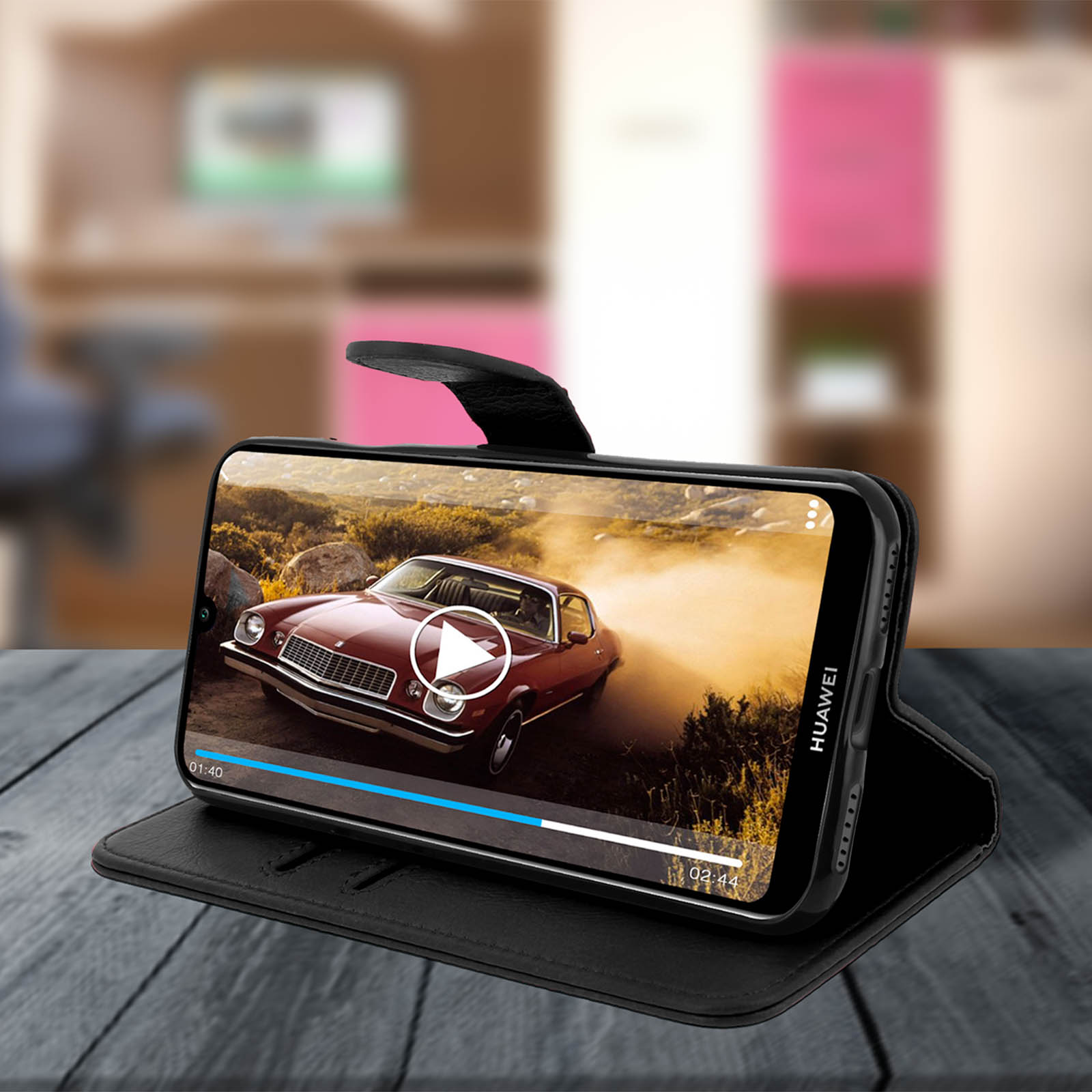Un telefono mostra un video di auto. Custodia nera su un tavolo di legno.