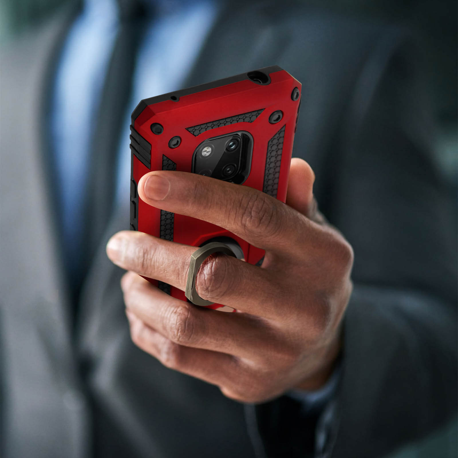 La main d'un homme tenant un étui de téléphone rouge et noir avec un support de bague. L'homme est en costume.