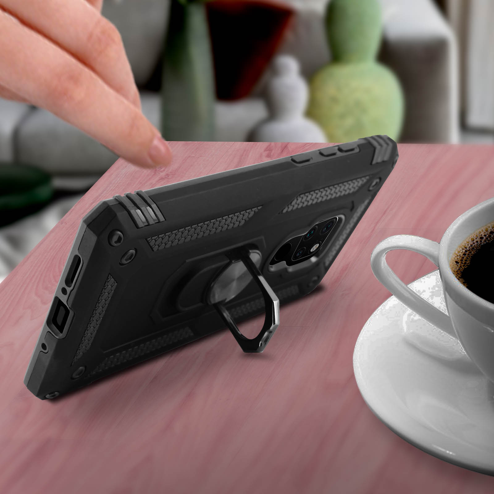 Zwarte telefoonhoes met een ringhouder, op een tafel. Een koffiekopje is zichtbaar.