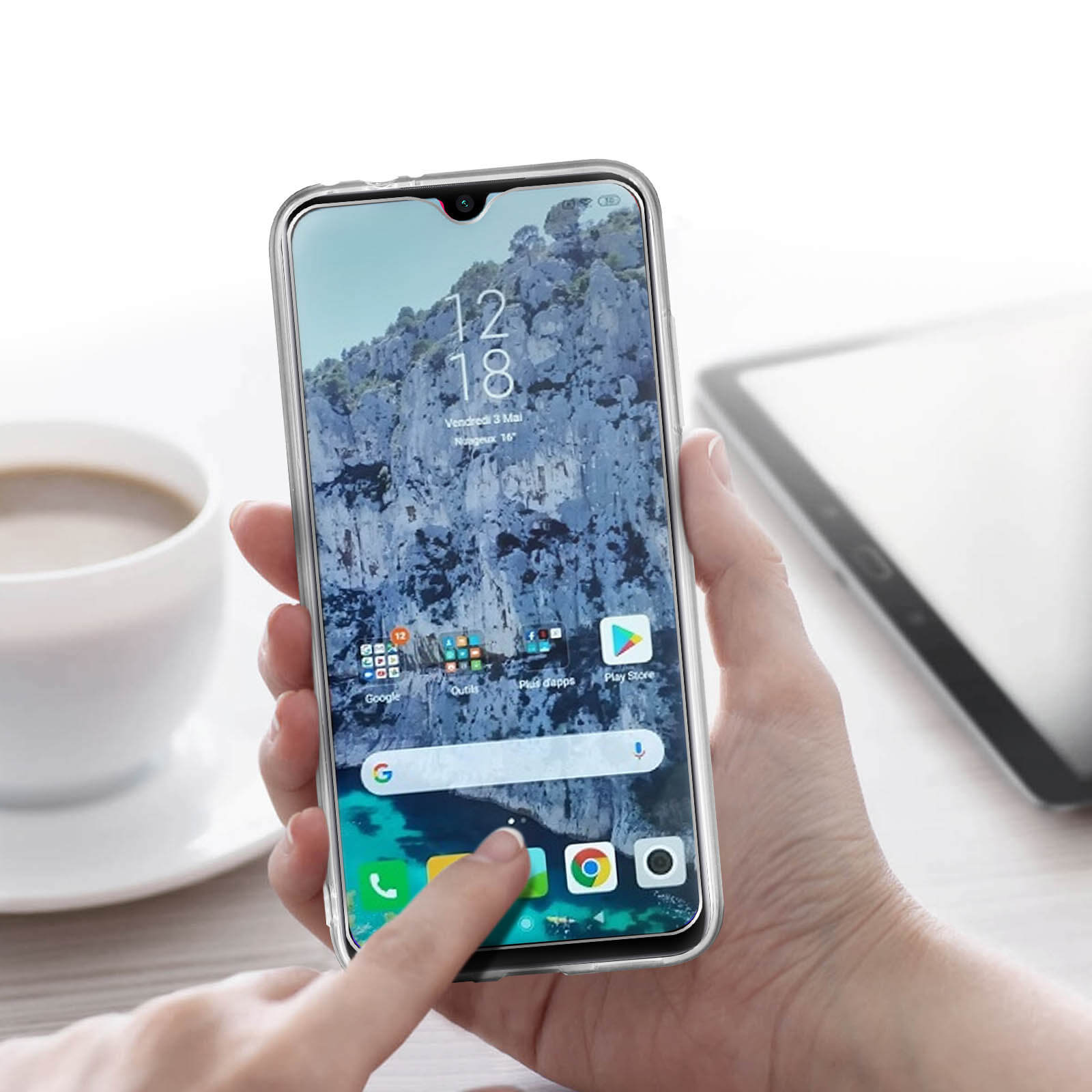 Mano che tiene un telefono con paesaggio montuoso, icone. Tazza di caffè e tablet visibili.