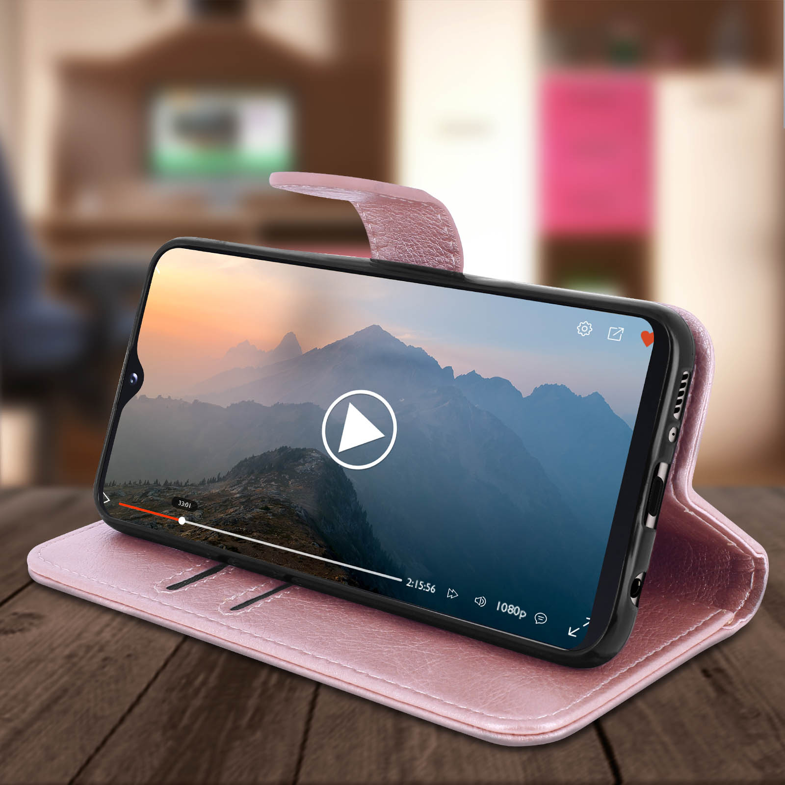 Roze telefoonhoes met een telefoon die een video afspeelt, op een houten tafel. Een woonkamer staat op de achtergrond.