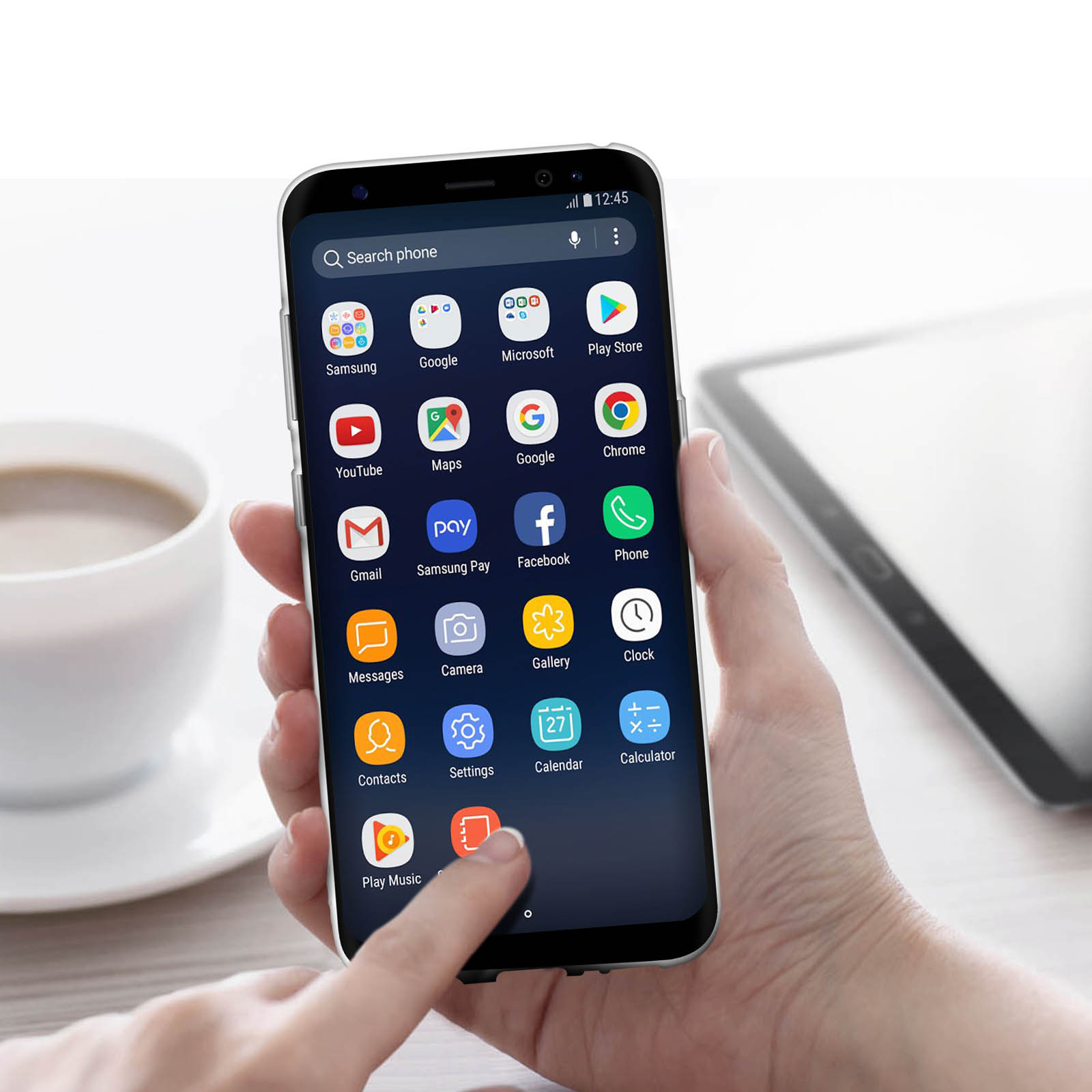 Eine Hand, die ein Telefon mit angezeigten App-Symbolen hält. Eine Kaffeetasse und ein Tablet im Hintergrund.
