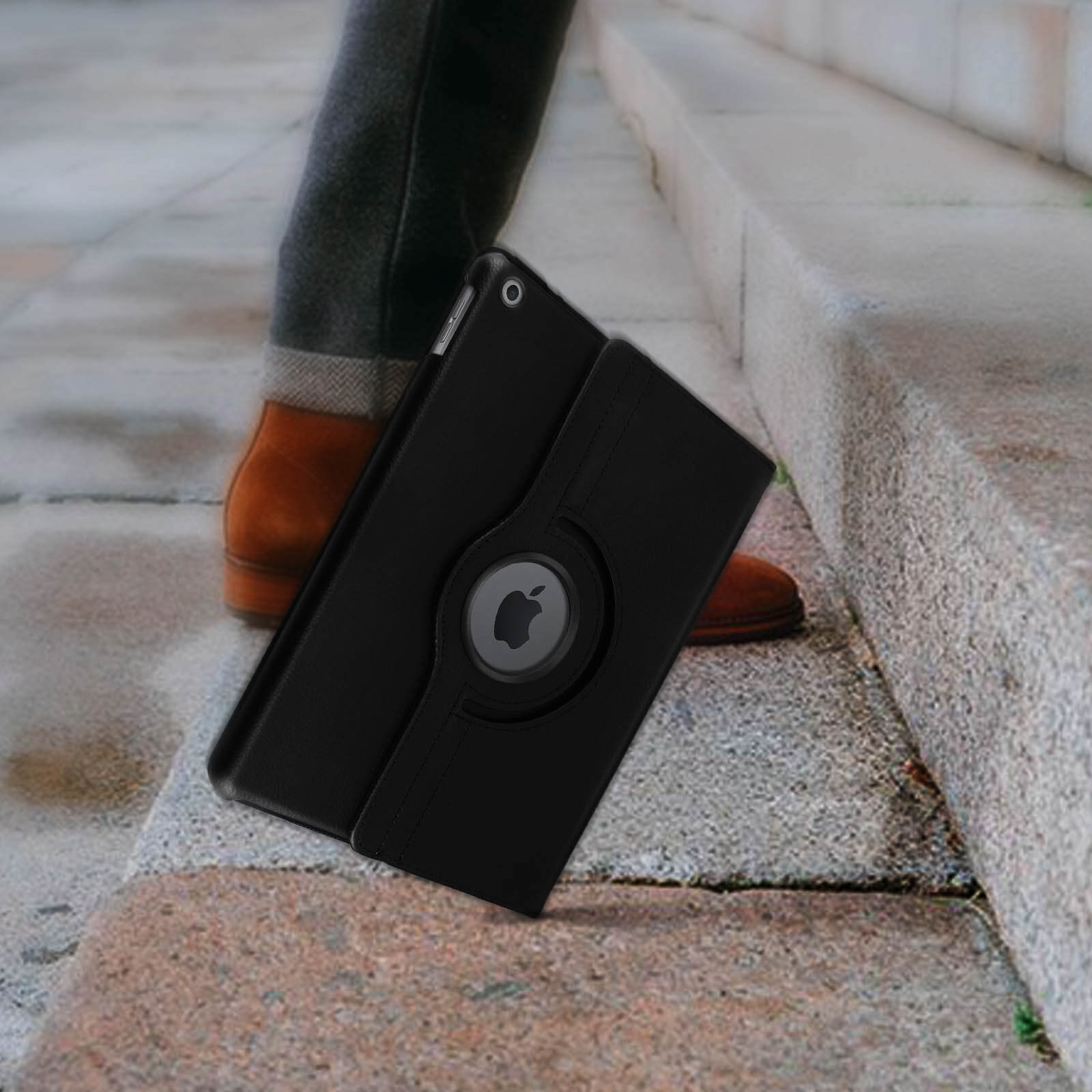 Custodia per tablet nera con logo Apple su gradino di pietra, gambe di persona sullo sfondo.
