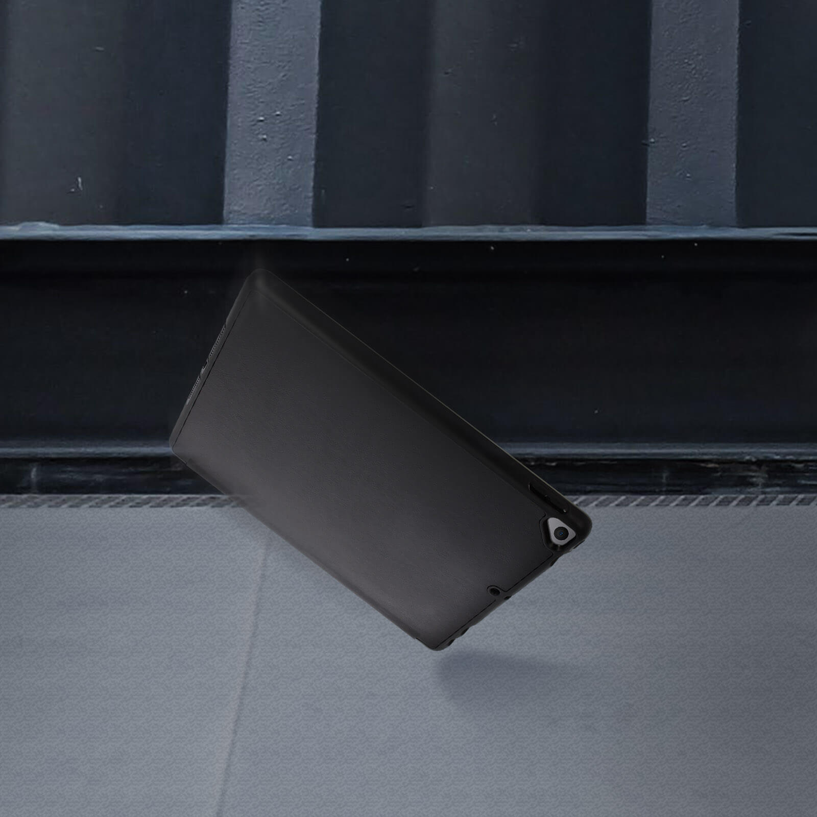 Una custodia per tablet nera che cade contro un muro e una superficie grigia.