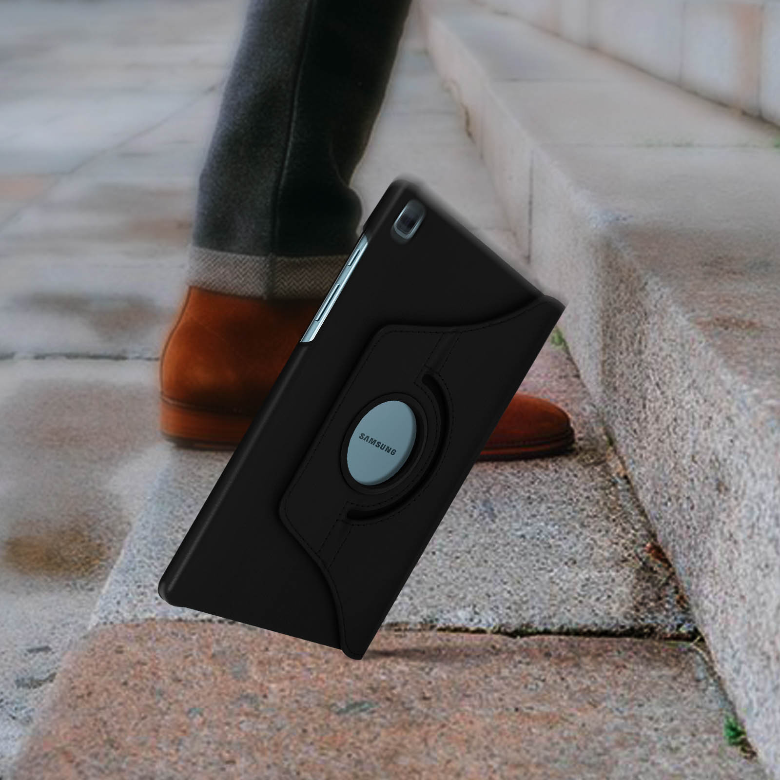 Un tablet in una custodia nera sta cadendo dalle scale. Si vedono le gambe di una persona e scarpe marroni.