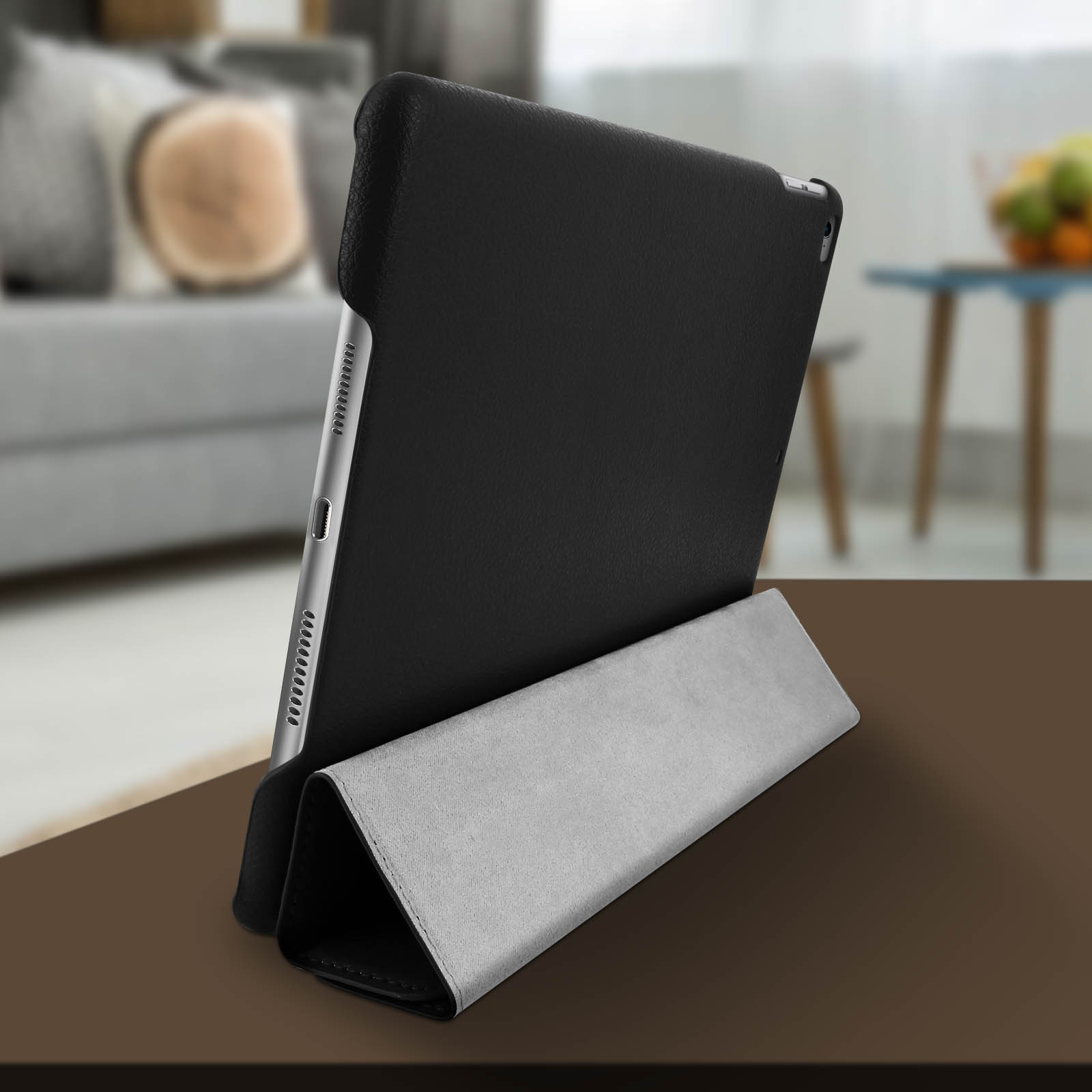 Custodia nera per iPad su supporto grigio. Sfondo: soggiorno sfocato.