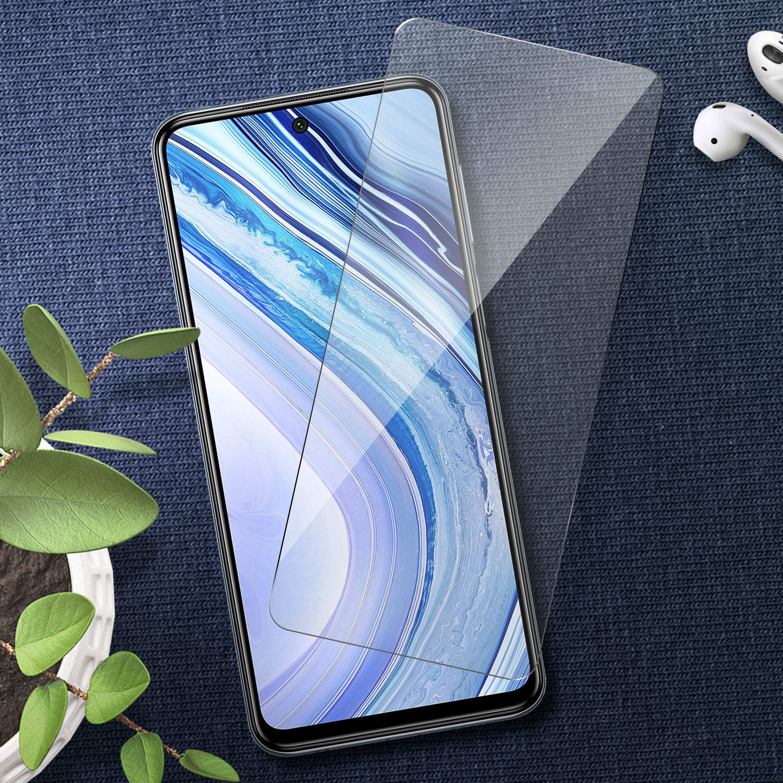 Téléphone avec protecteur d'écran et écouteurs sur surface bleue à motifs, près d'une plante.