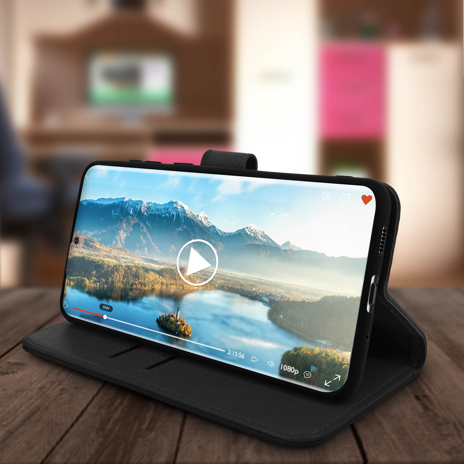 Téléphone noir dans un étui, affichant une vidéo sur une table en bois. Arrière-plan flou.