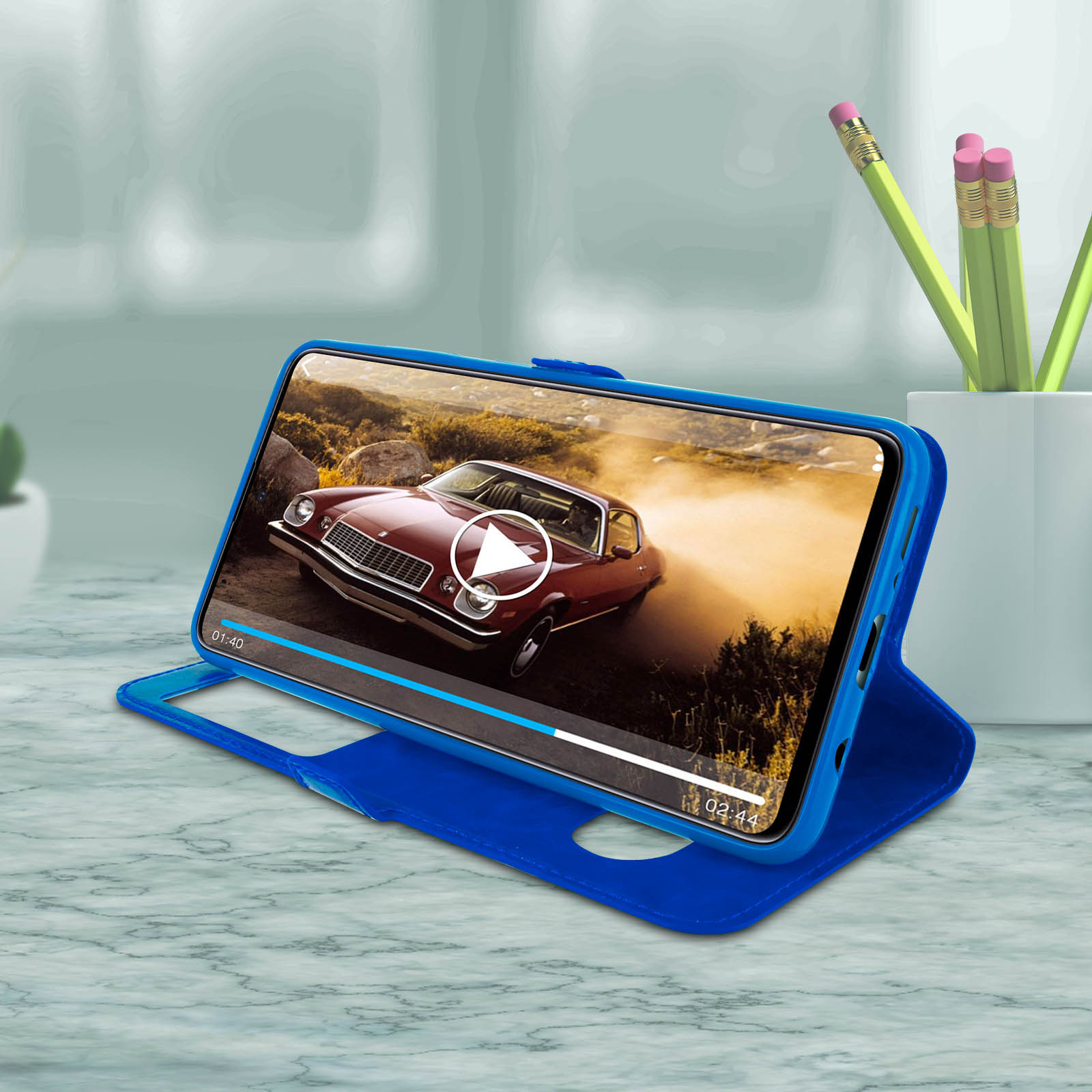 Un telefono in una custodia blu, che riproduce un video di un'auto rossa su un tavolo di marmo.