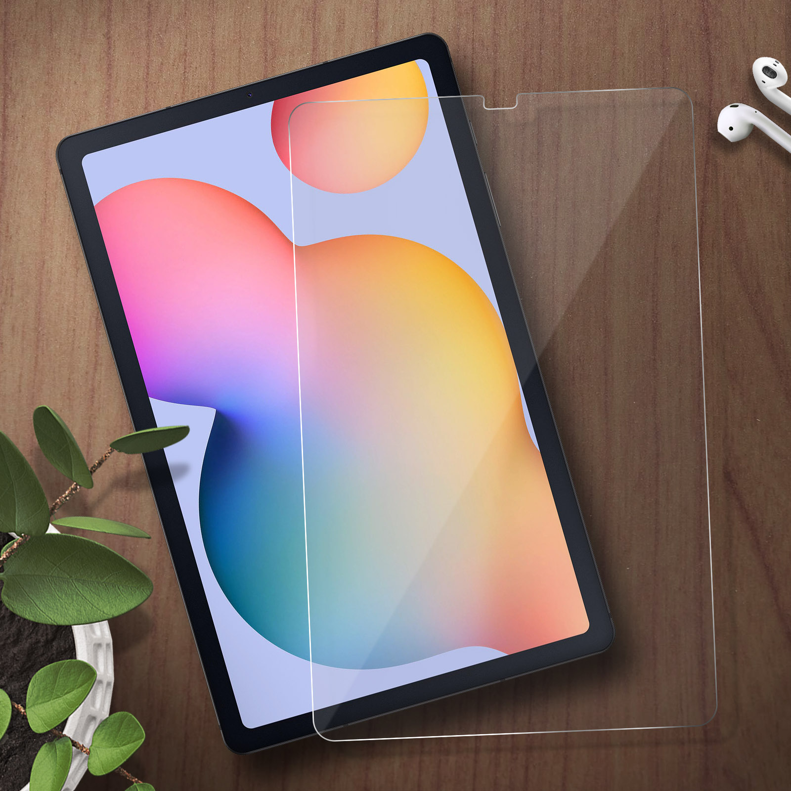 Un tablet e una protezione schermo su un tavolo di legno accanto a una pianta e auricolari bianchi.