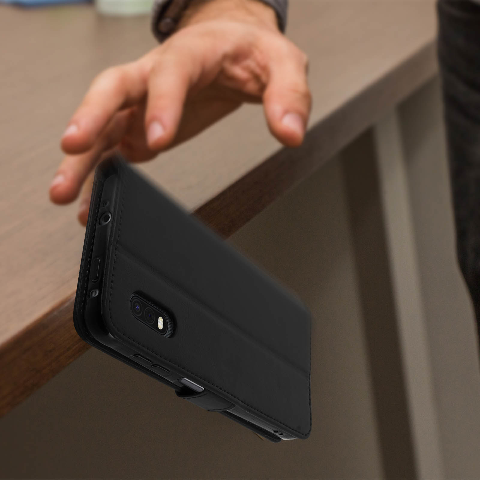 Una mano che si avvicina a una custodia nera per telefono posta su una superficie di legno.