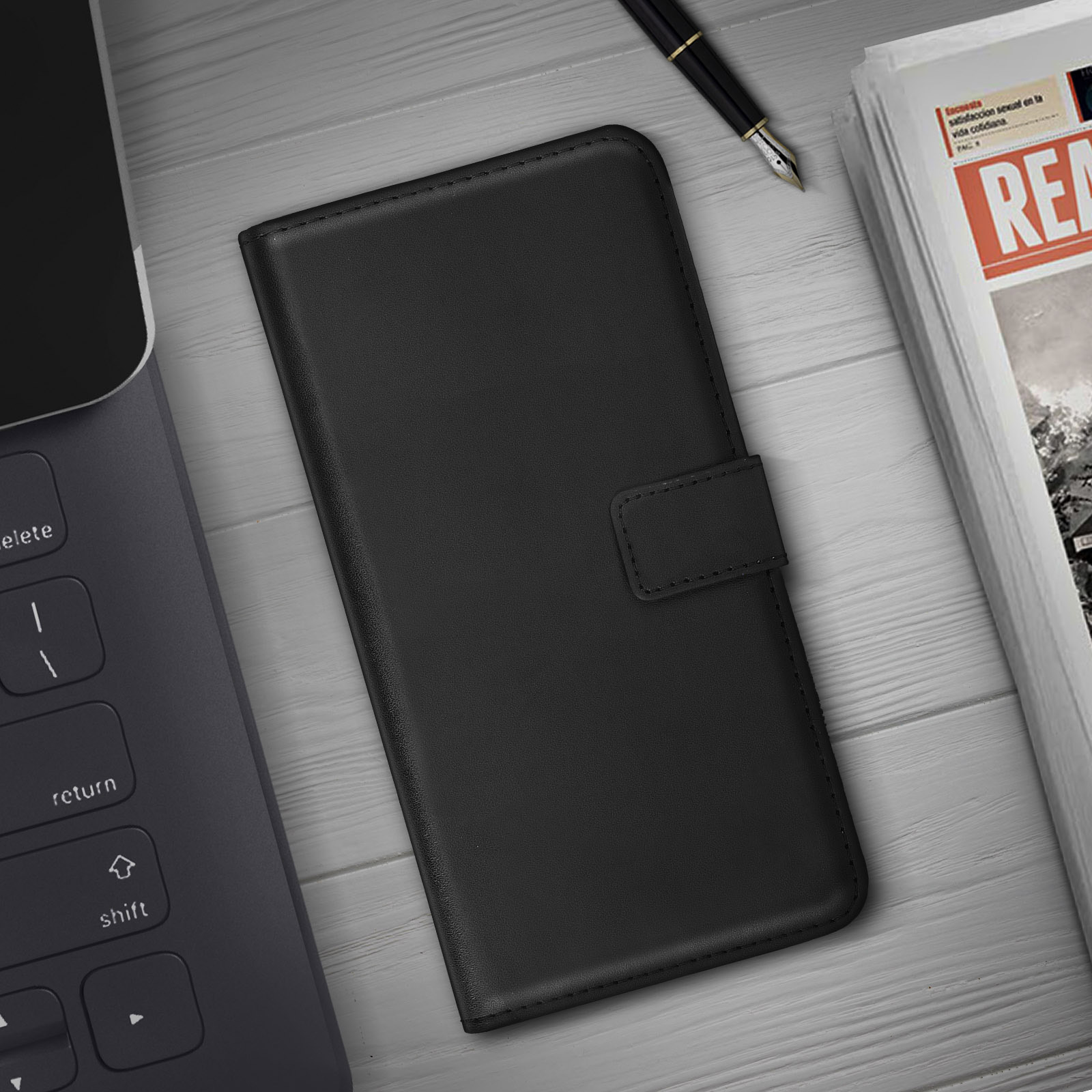 Étui de téléphone noir fermé sur une table en bois, avec un stylo et un journal en arrière-plan.