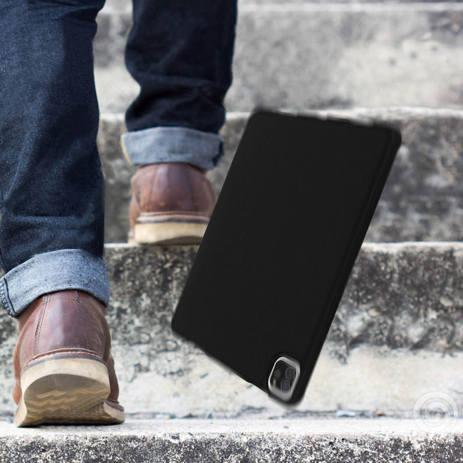 Una custodia nera per tablet vicino alle scale, con gambe e scarpe sullo sfondo.