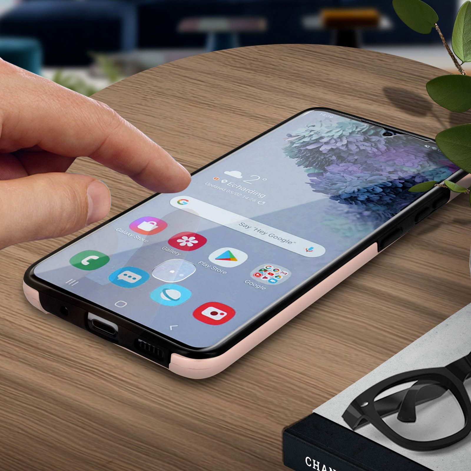 Hand die een telefoonscherm aanraakt. Telefoon ligt op een houten tafel, in de buurt van een bril en een plant.