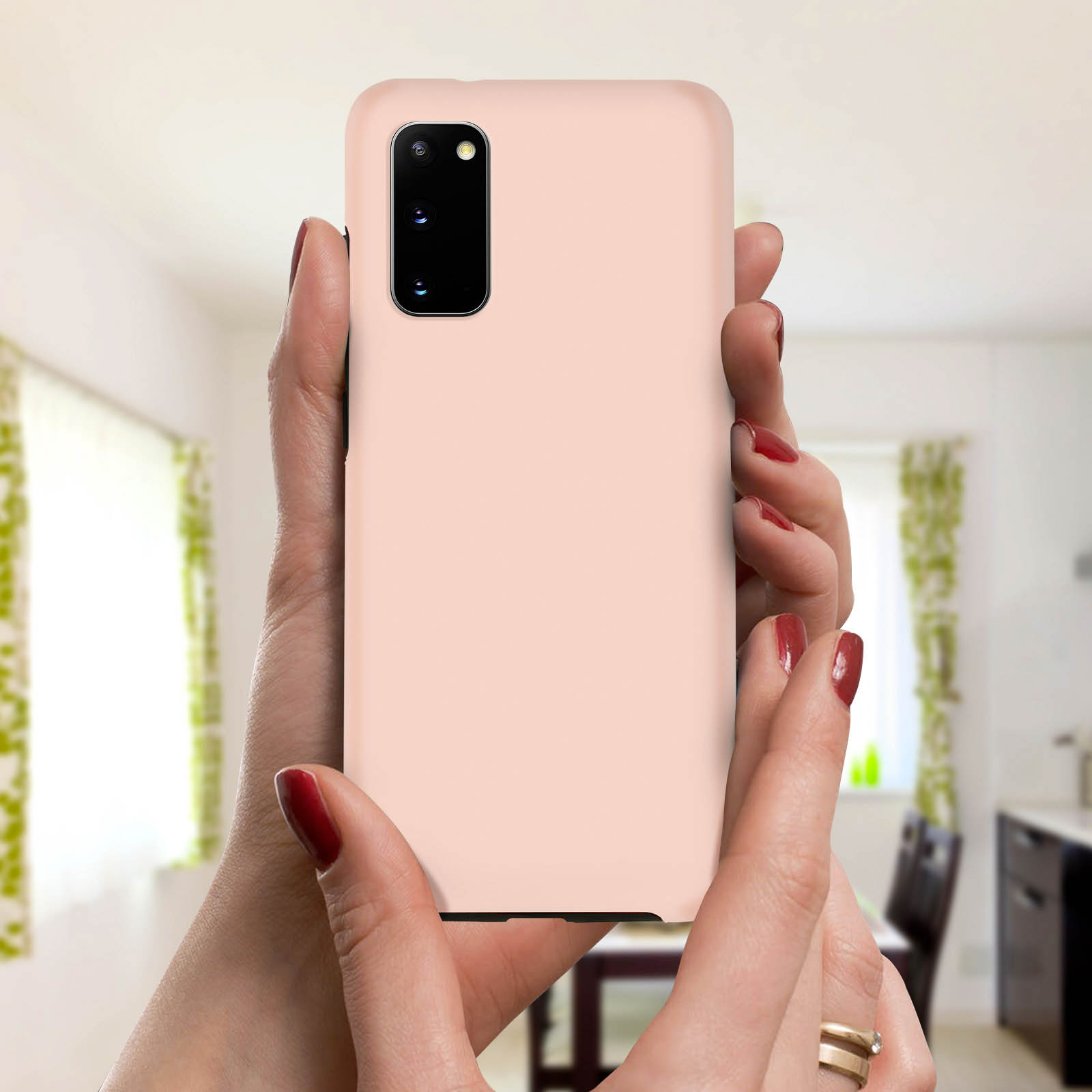 Handen die een roze telefoon vasthouden. Rode nagellak. Vage achtergrond met kamer en gordijnen.