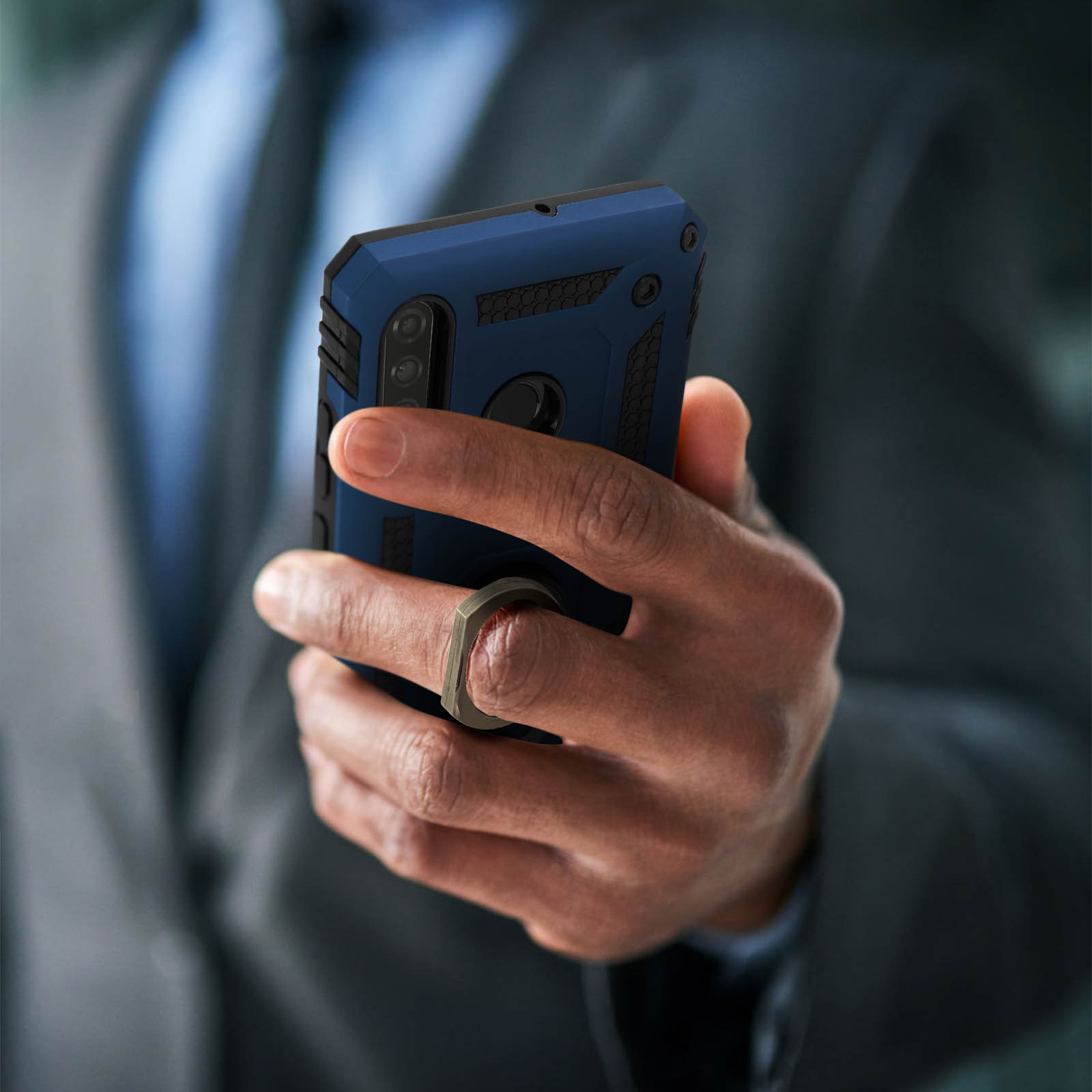 Homme en costume tenant une coque de téléphone bleue. Anneau. Téléphone noir. Arrière-plan flou.