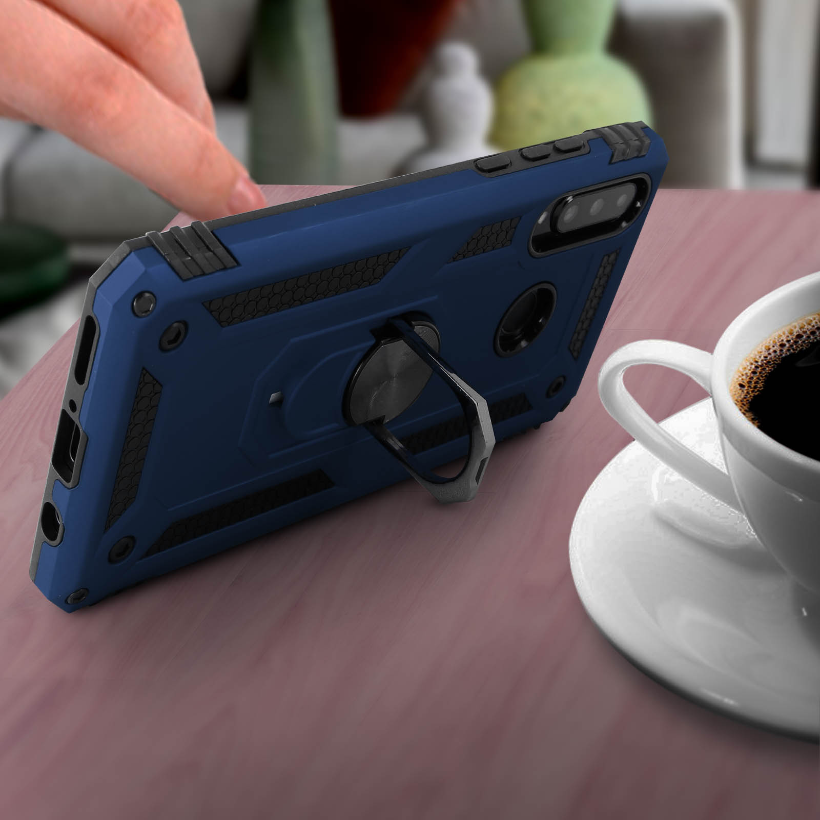 Un étui de téléphone bleu avec un support annulaire. Une tasse de café sur une table à proximité.