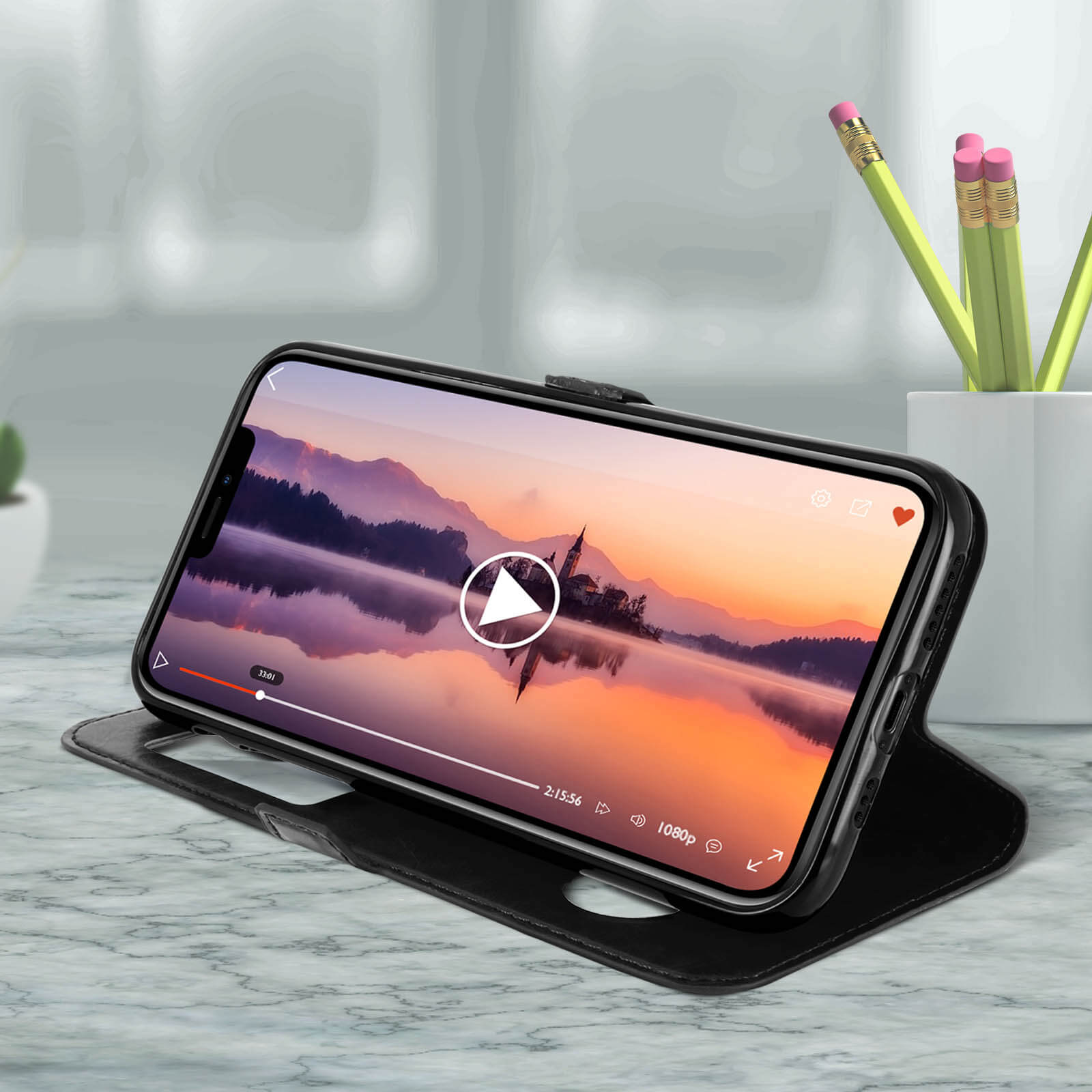 Telefono in una custodia nera che mostra un video del tramonto. Il telefono è su un tavolo con matite.