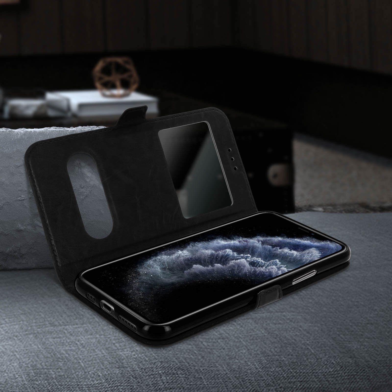 Custodia per telefono in pelle nera con un telefono all'interno, aperta su una superficie grigia. Sfondo scuro.