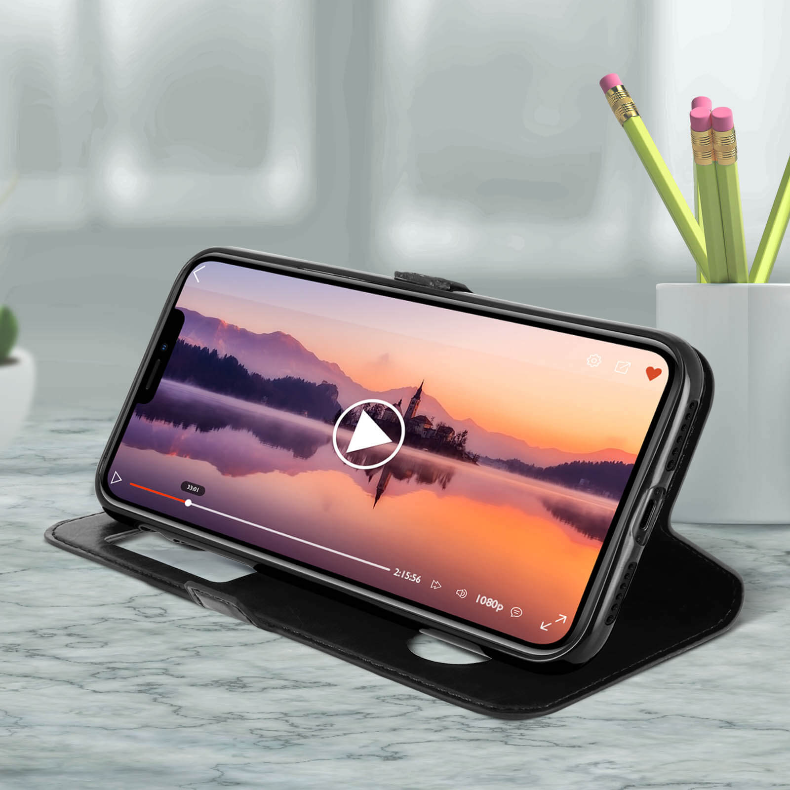 Een telefoon in een zwarte hoes toont een video van een zonsondergang. De hoes is open op een marmeren oppervlak.