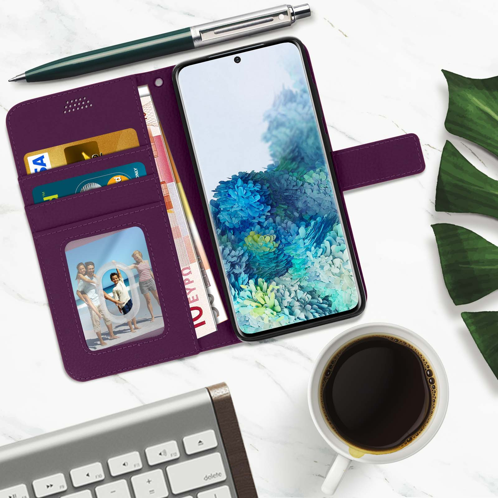 Custodia per telefono viola, denaro, penna, caffè e una foto. Sono presenti anche una tastiera e foglie.