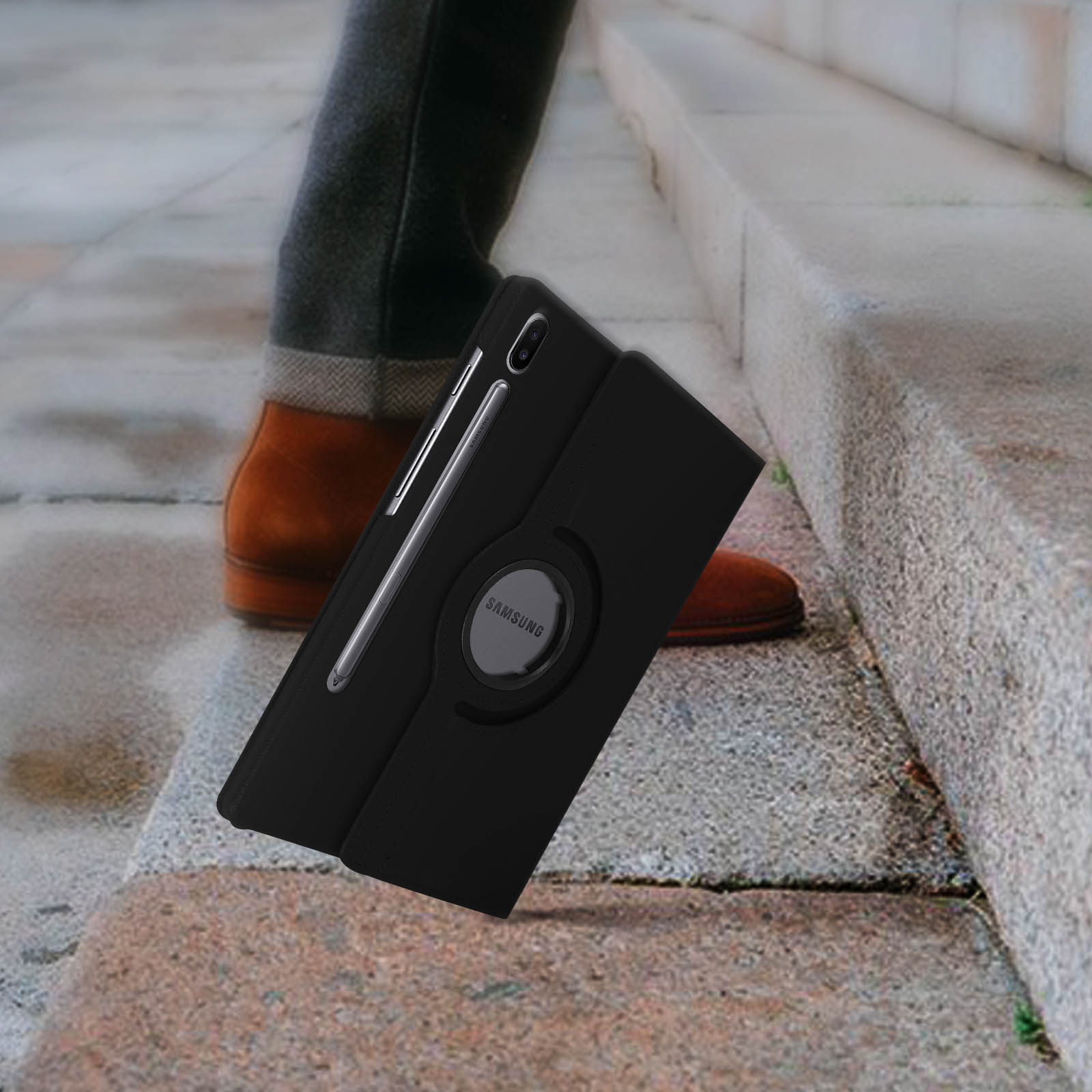 Custodia nera per tablet con pennino e supporto ad anello. Le gambe e le scarpe di una persona sono visibili sullo sfondo di una scala.