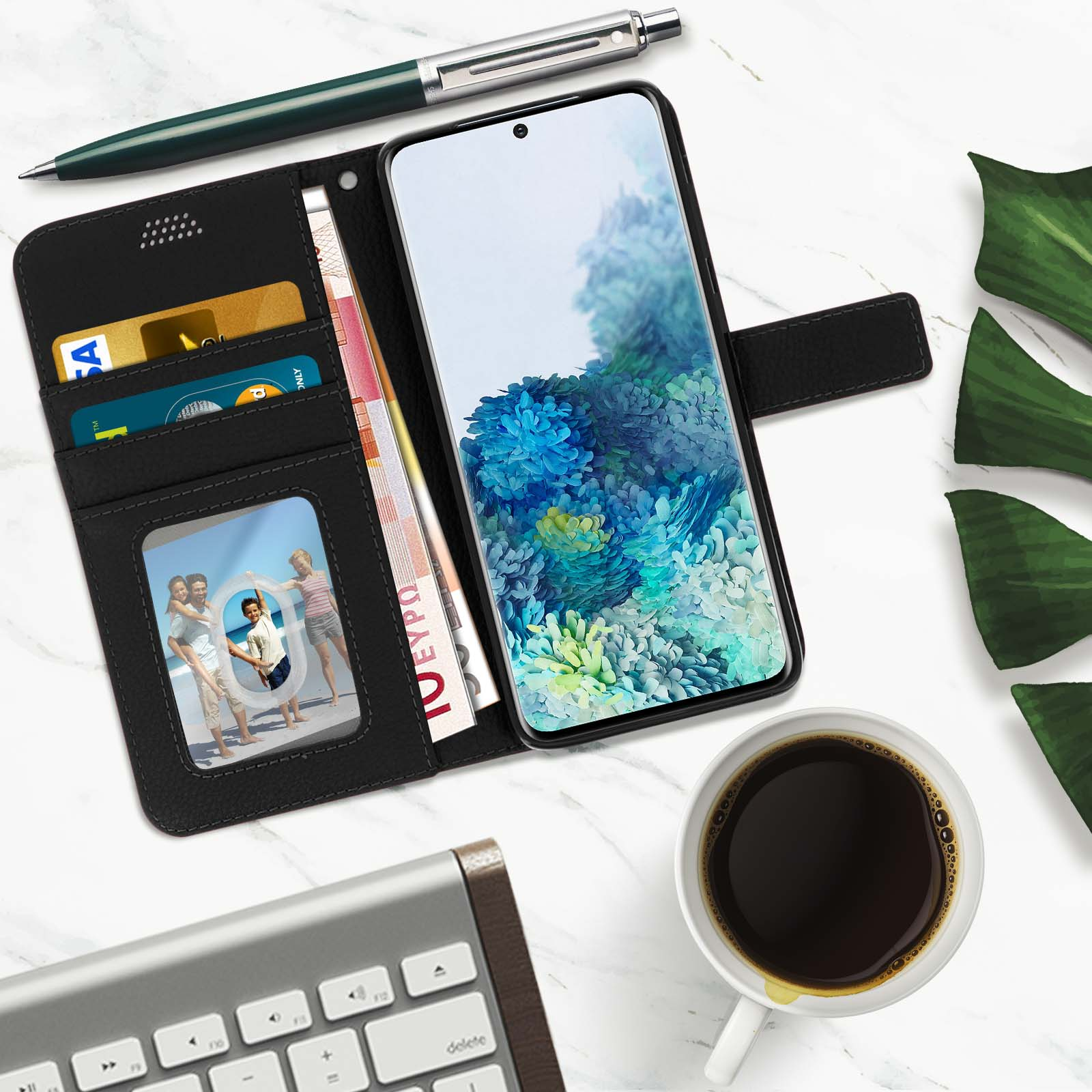 Telefono in custodia a portafoglio, con denaro, carte e foto. Caffè e penna su superficie di marmo.