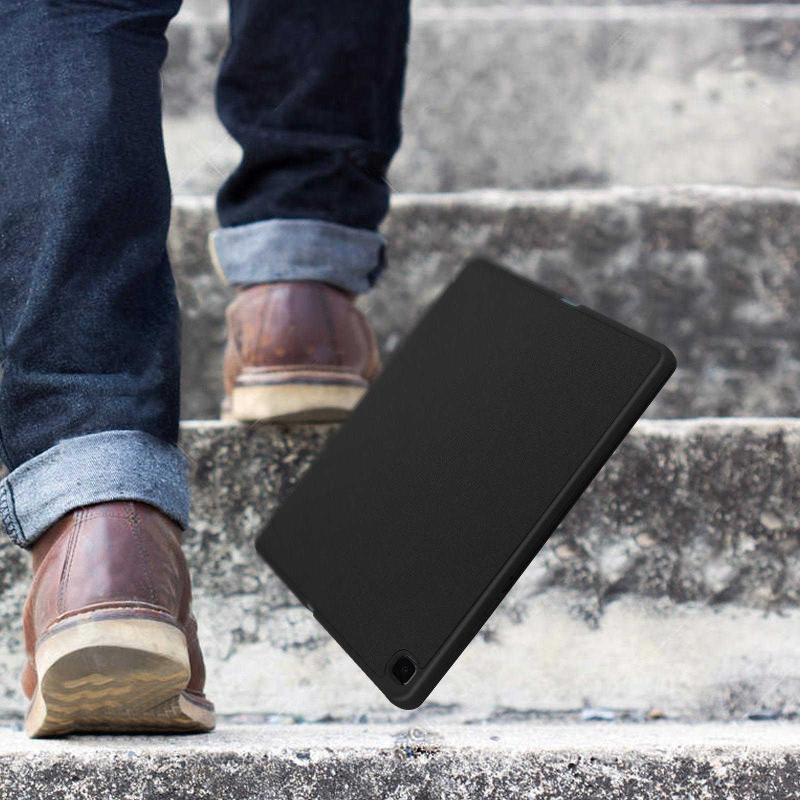 Gambe di una persona che sale le scale. Una custodia nera per tablet è sulle scale.