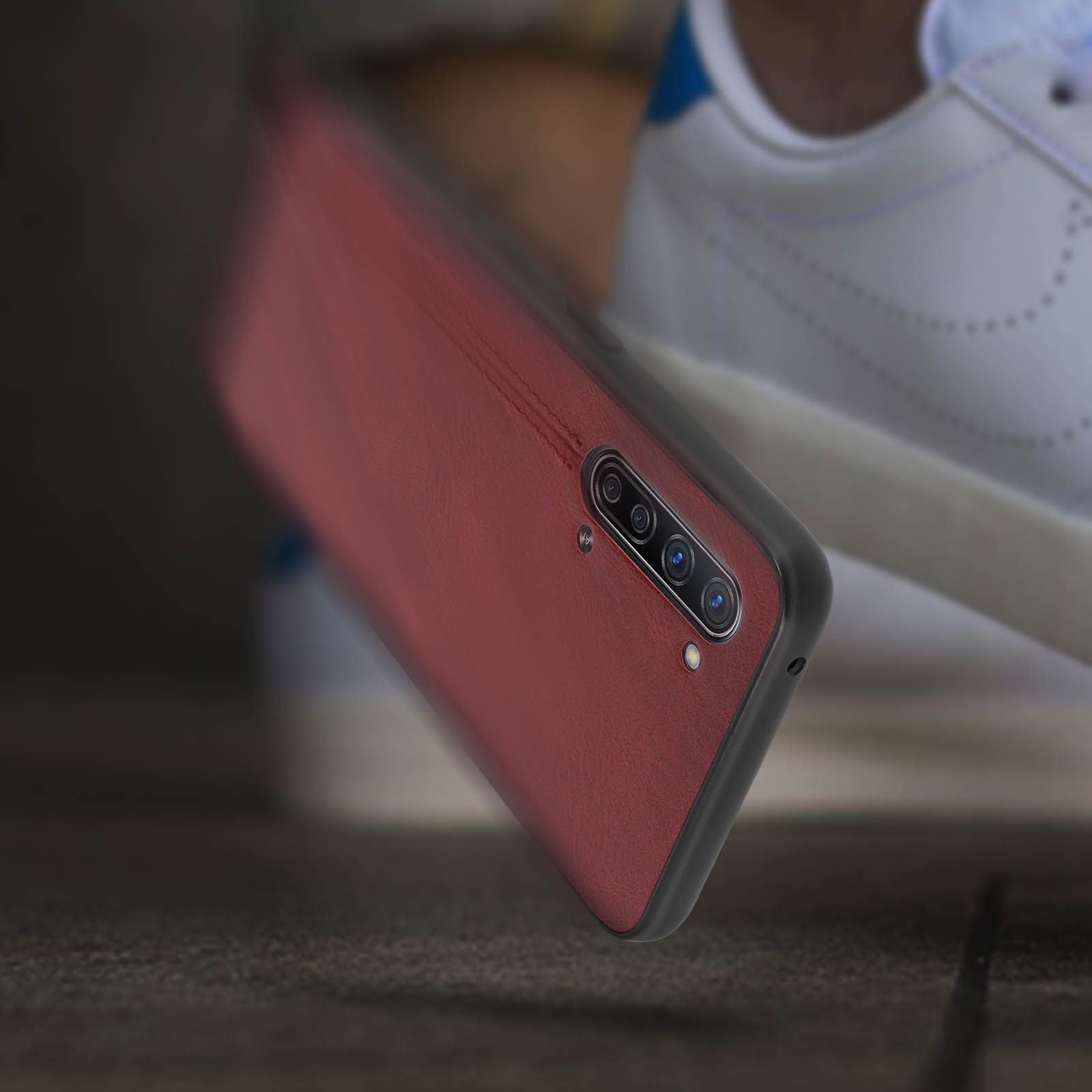 Custodia per telefono rossa che cade. Le lenti della fotocamera sono visibili. La superficie è in legno. Dettagli neri.