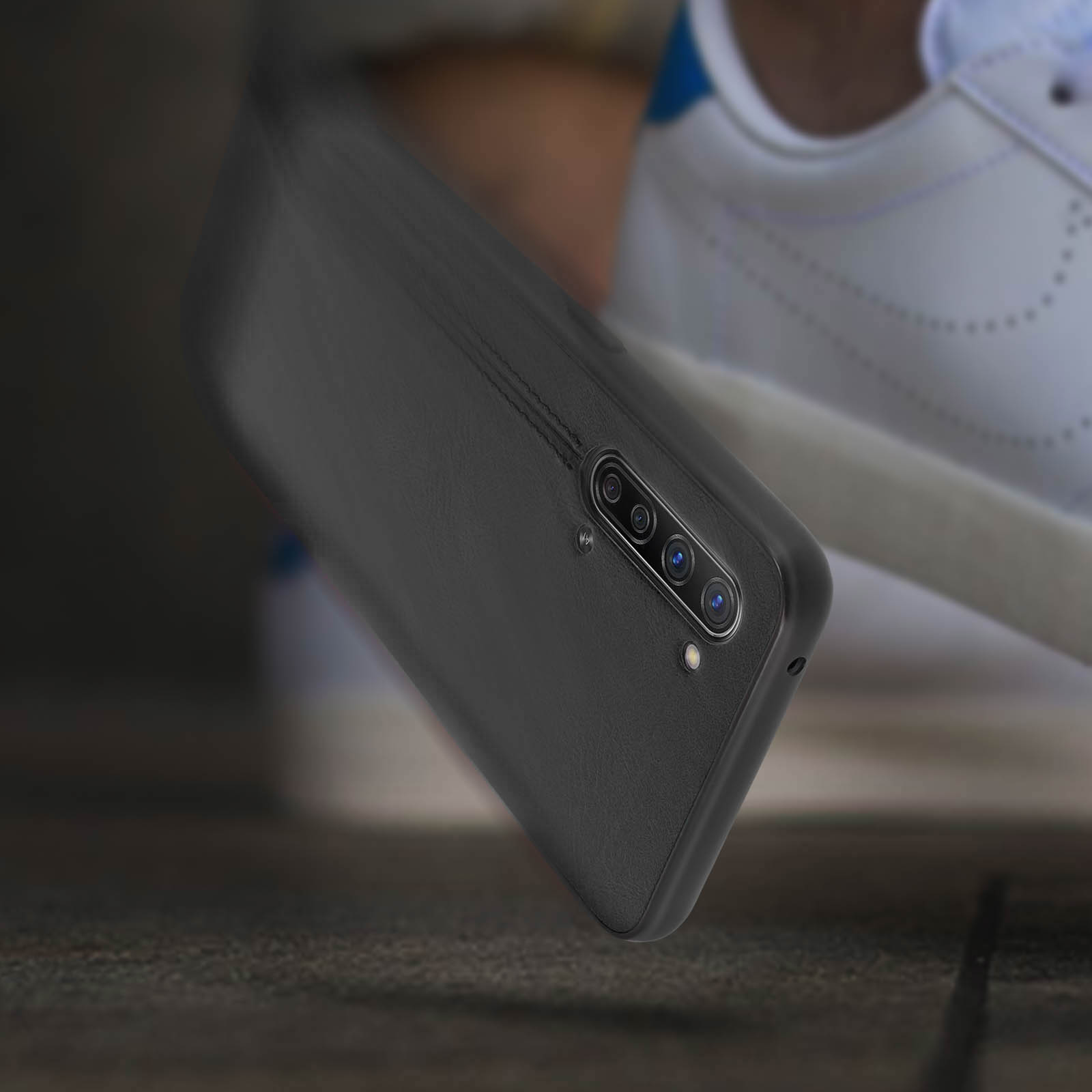 Custodia nera per telefono con design strutturato. Una sneaker sullo sfondo.