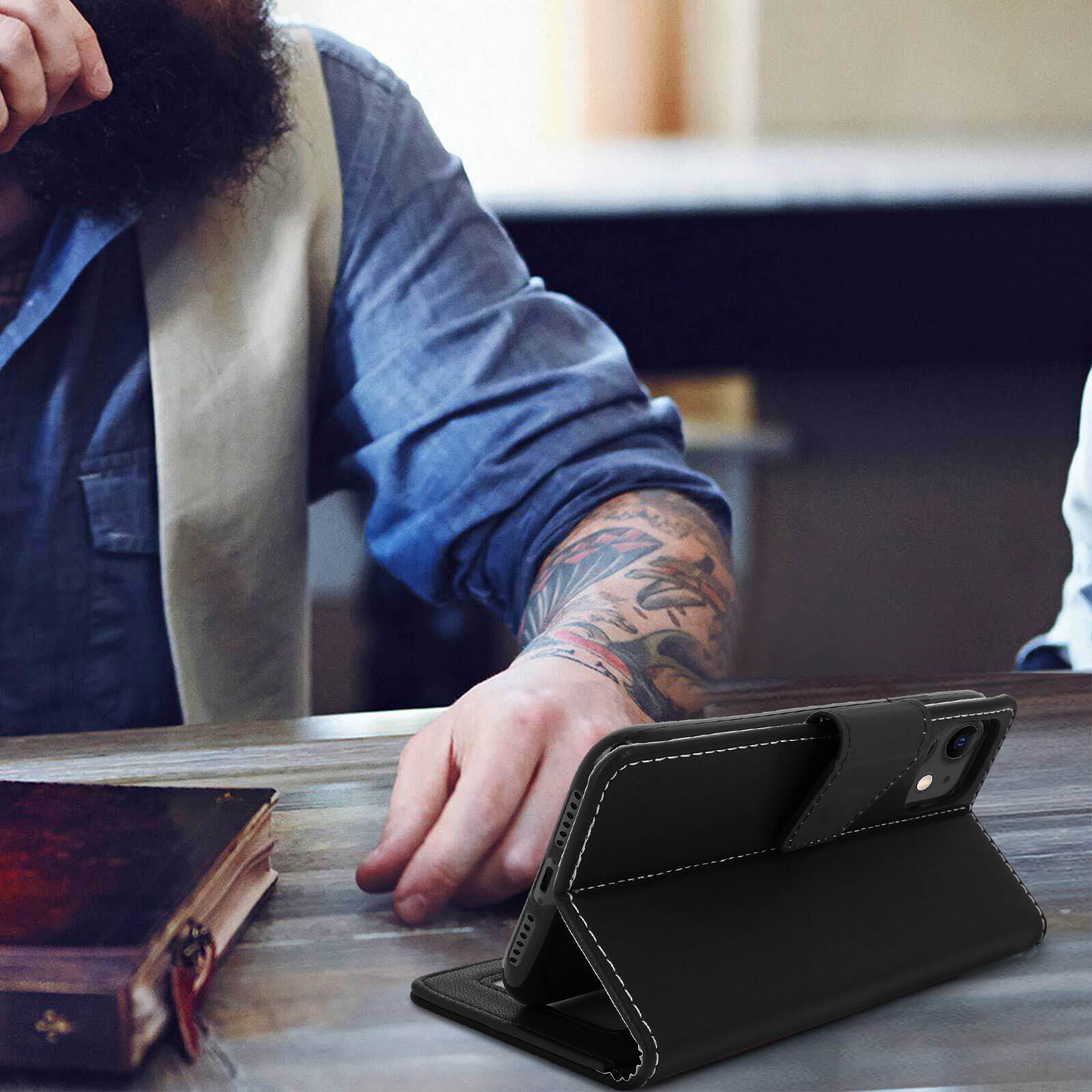 Uomo con tatuaggi sulle maniche usa telefono in custodia nera con cuciture bianche.