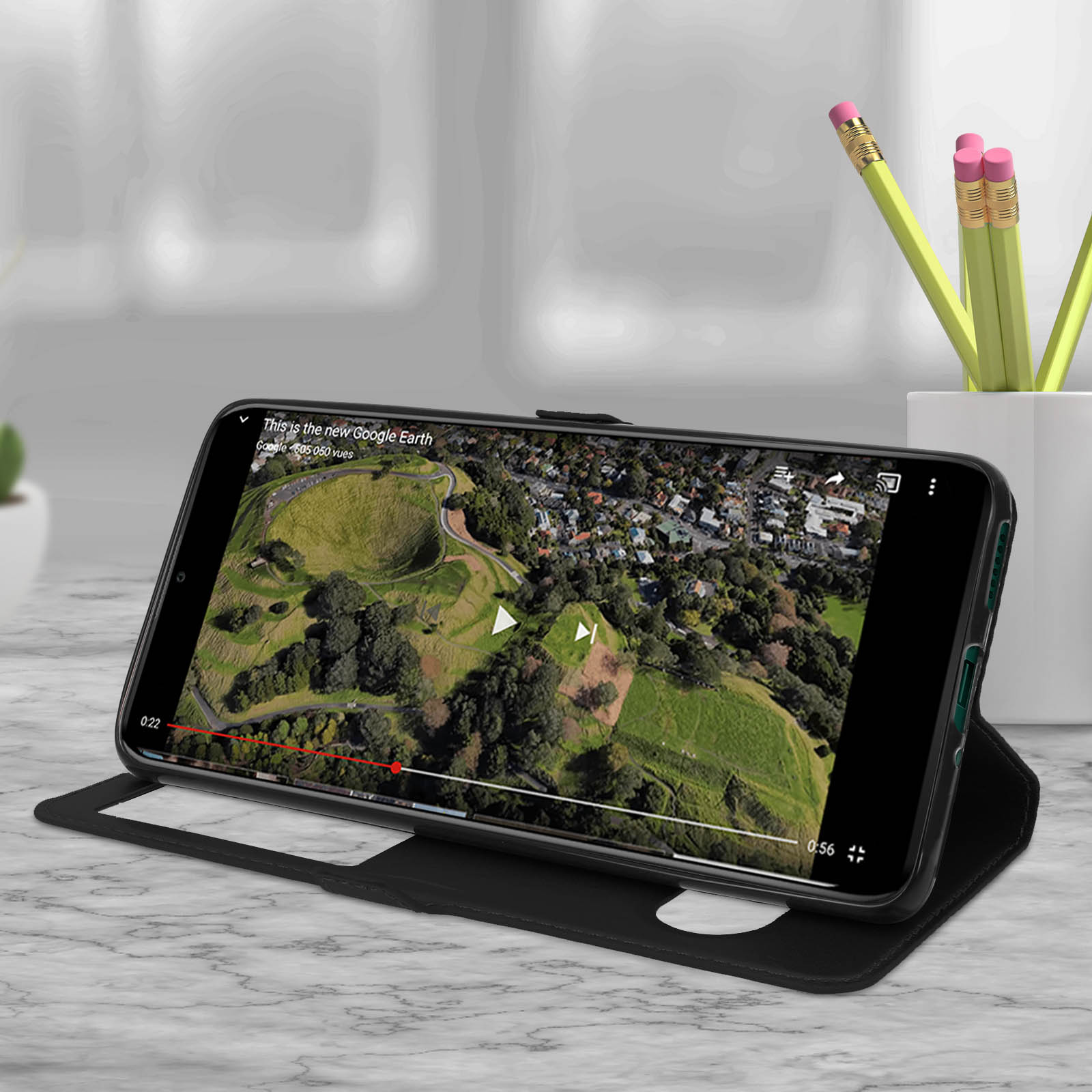 Un téléphone portable lit une vidéo sur un étui noir. La vidéo montre une vue de drone d'un paysage vert.