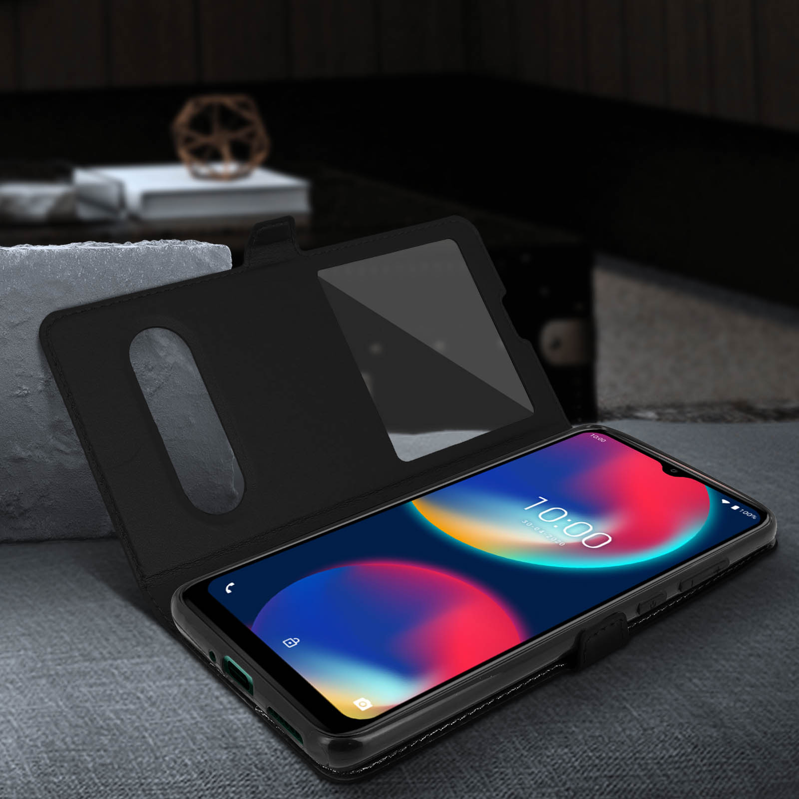 Une coque de téléphone noire, ouverte, montrant un téléphone avec un écran coloré. L'étui est sur une surface grise.