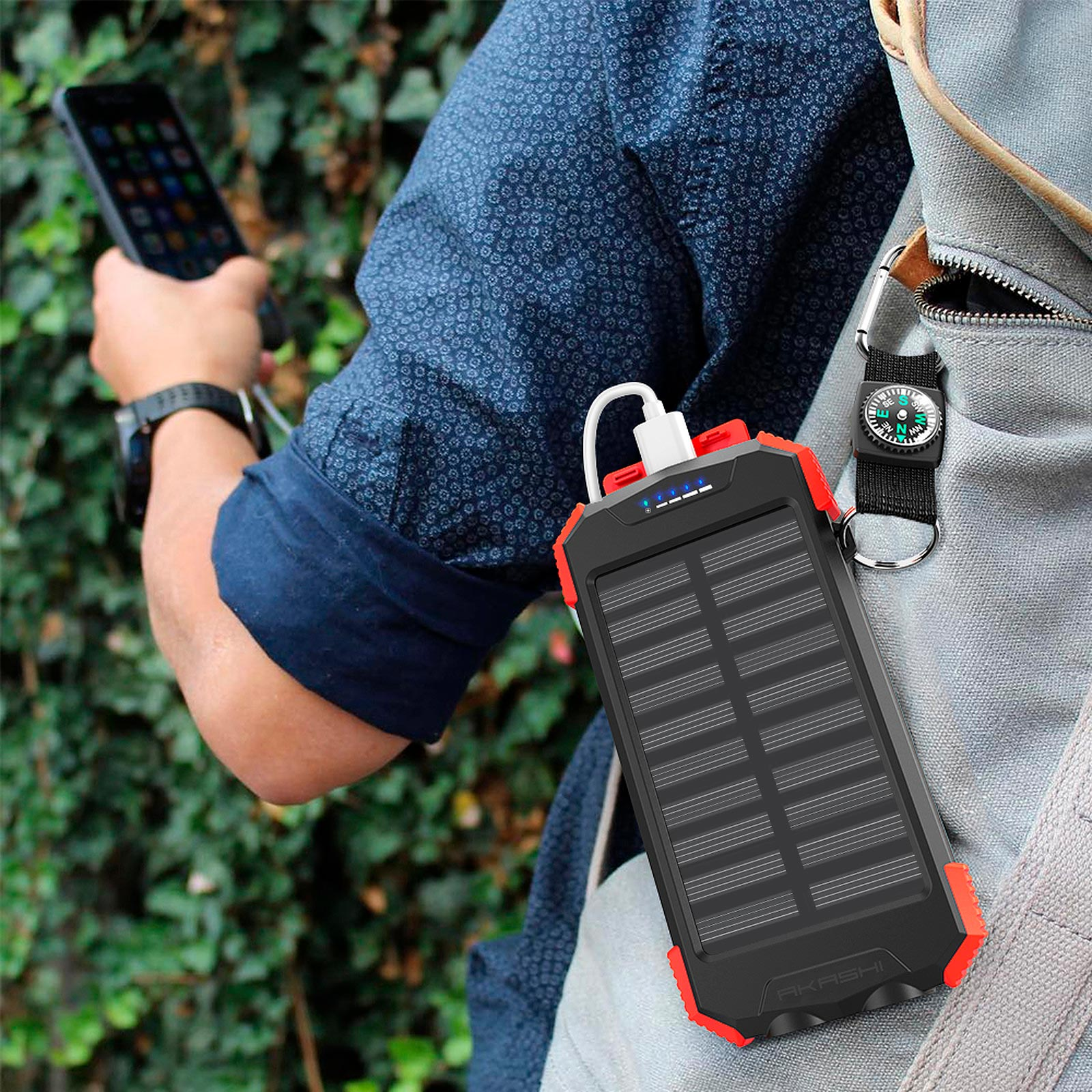 Mann, der ein Telefon hält, eine Powerbank mit Solarpanel und einen Kompass auf einem Rucksack.