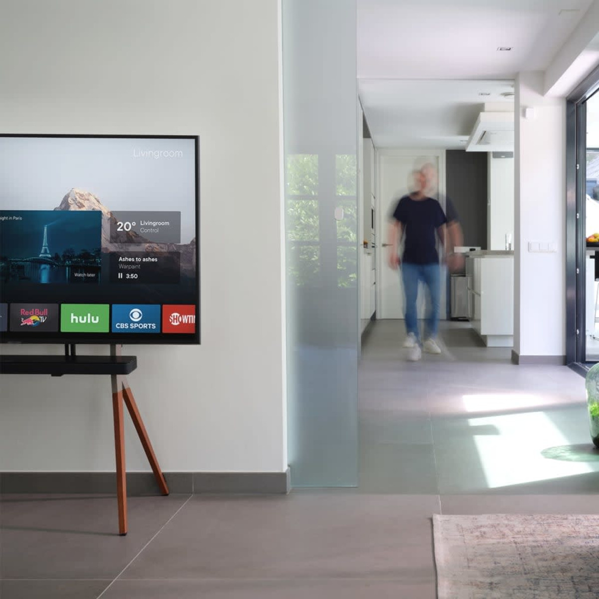 Fernseher auf einem Ständer zeigt Apps. Mann geht im Hintergrund. Der Raum hat modernes Design mit weißen Wänden.