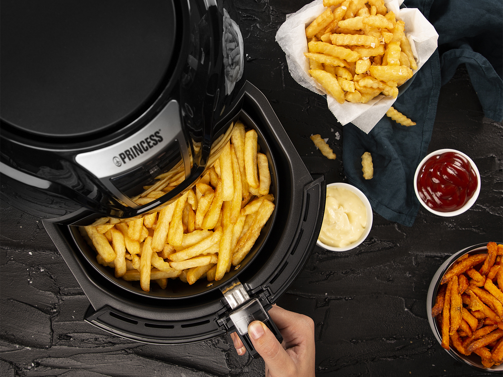 Koszyk frytkownicy wypełniony frytkami. Ketchup i majonez w małych miseczkach w pobliżu.