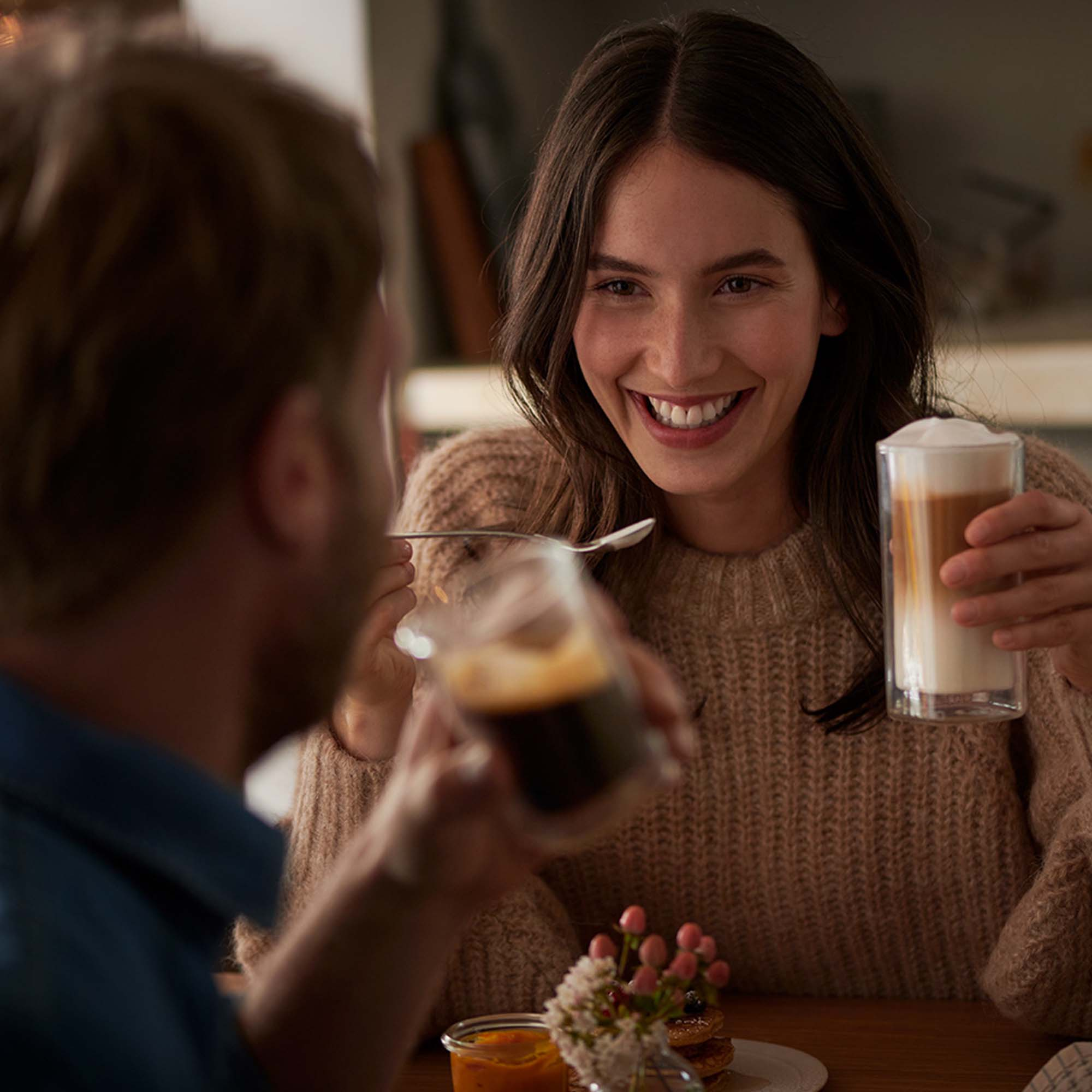 Frau lächelt und hält Latte. Ein Mann hält ein dunkles Getränk.