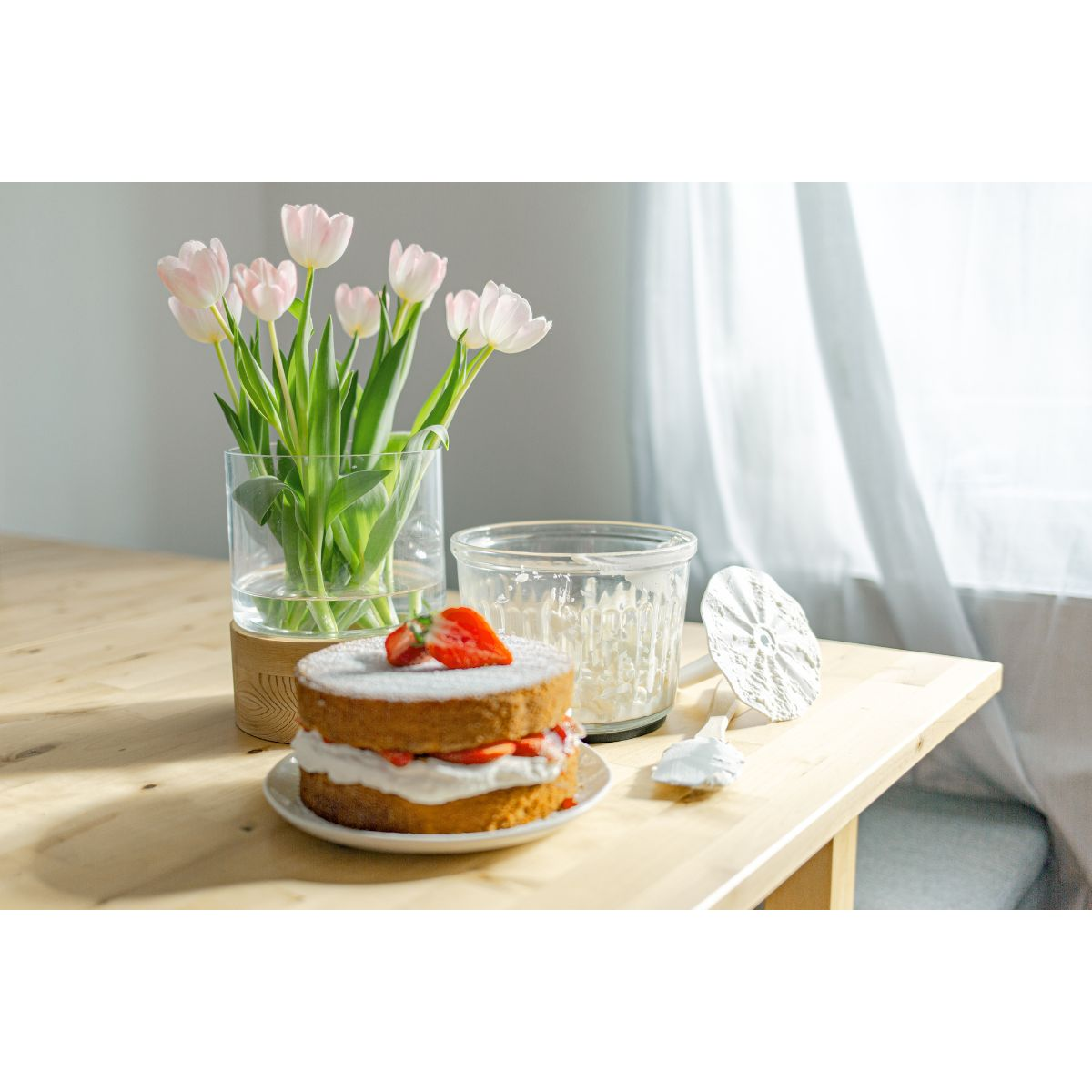 Pastel de fresas, jarrón con tulipanes rosas, portavelas de cristal, sobre una mesa de madera.