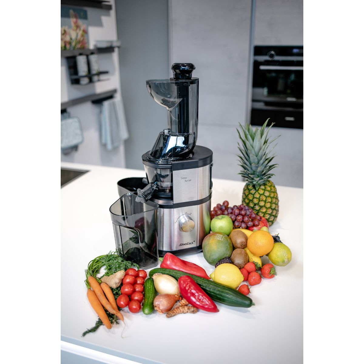 Exprimidor rodeado de frutas y verduras. Piña, manzana y otros productos visibles.