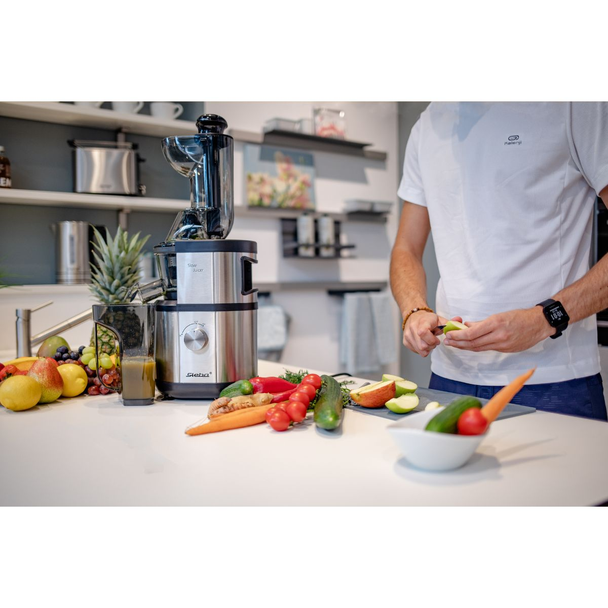 Un hombre está cortando una manzana y preparando verduras. Una exprimidora está detrás de ellos.