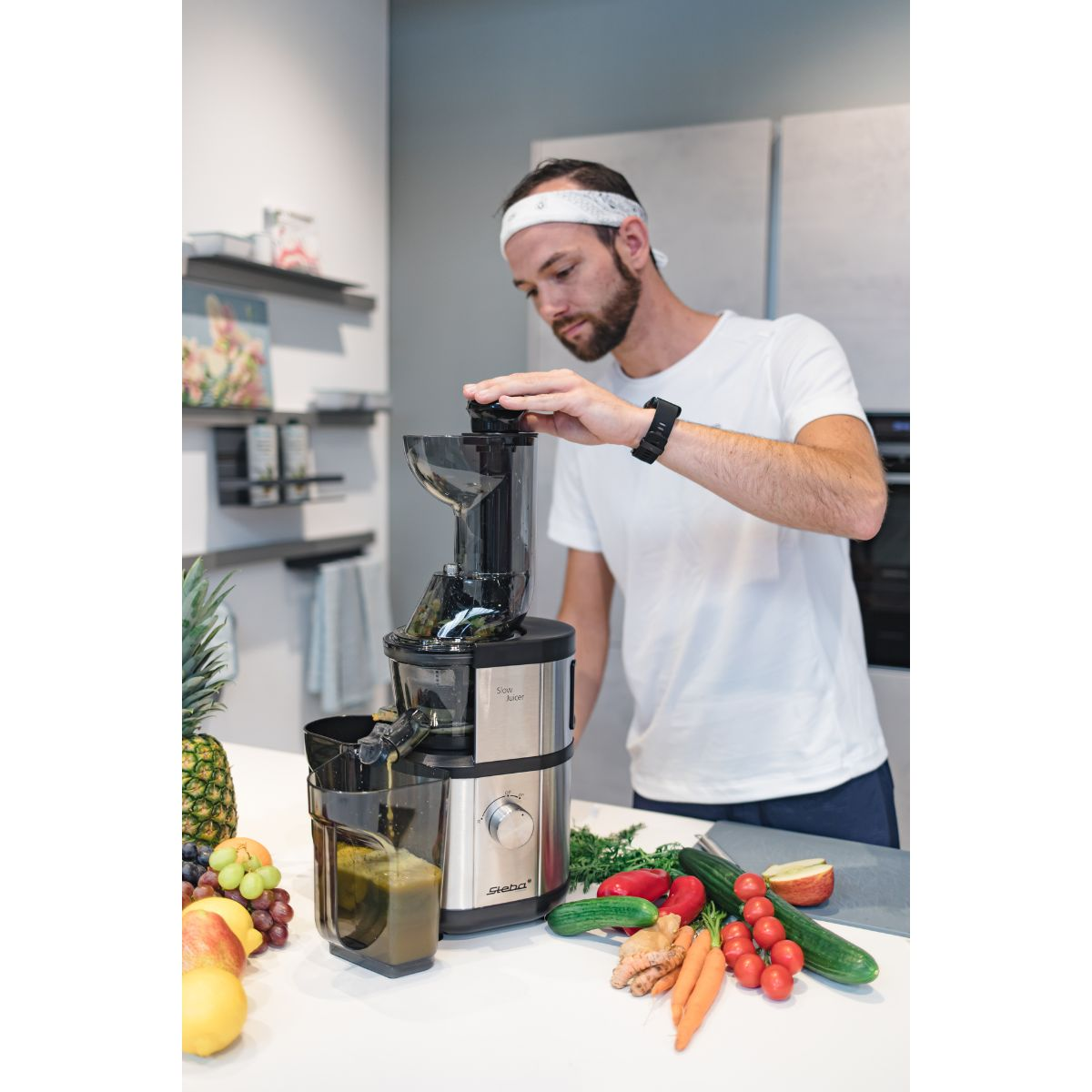 Hombre usando una exprimidora. Frutas y verduras en la encimera.