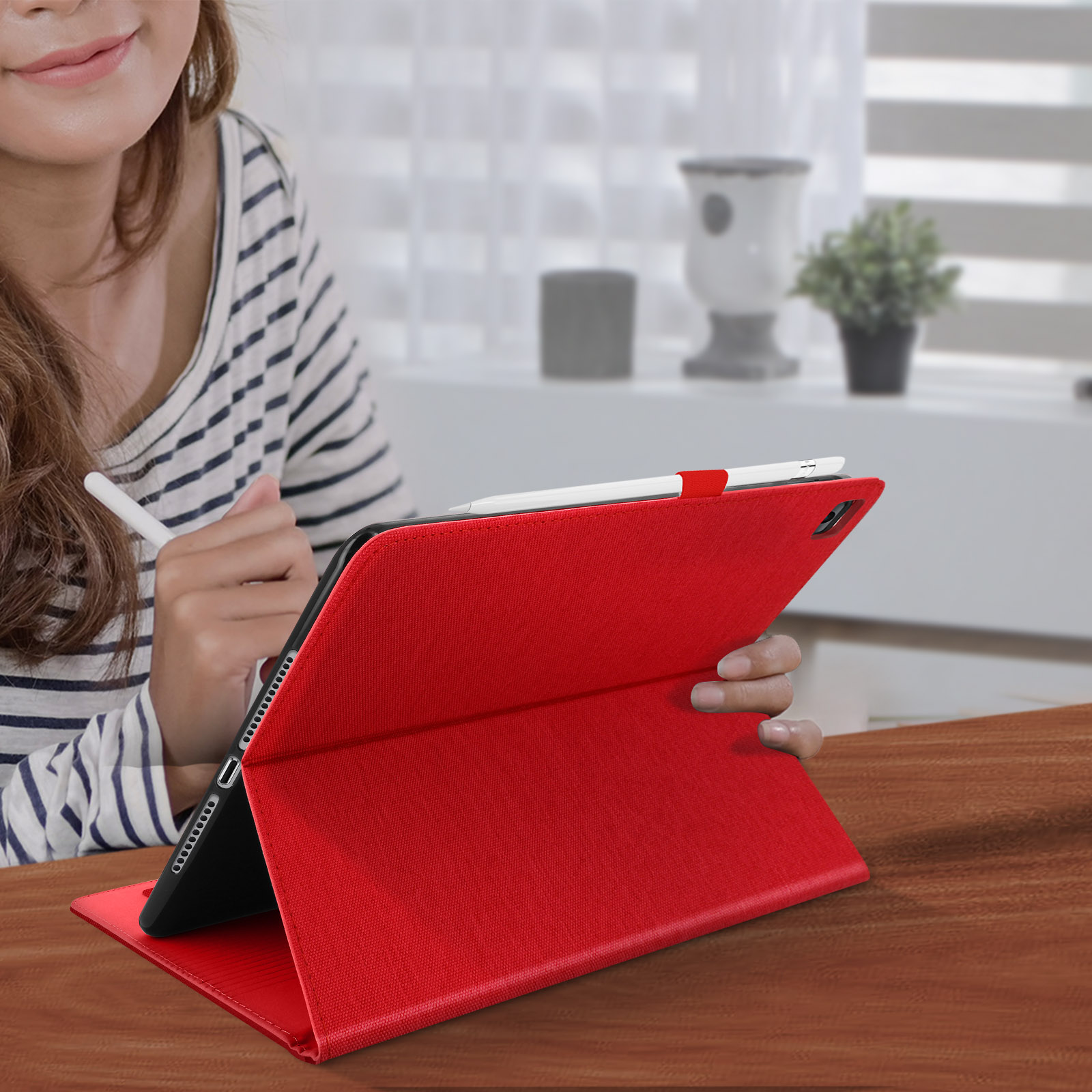 Una persona che tiene una custodia per tablet rossa con una matita su un tavolo di legno.