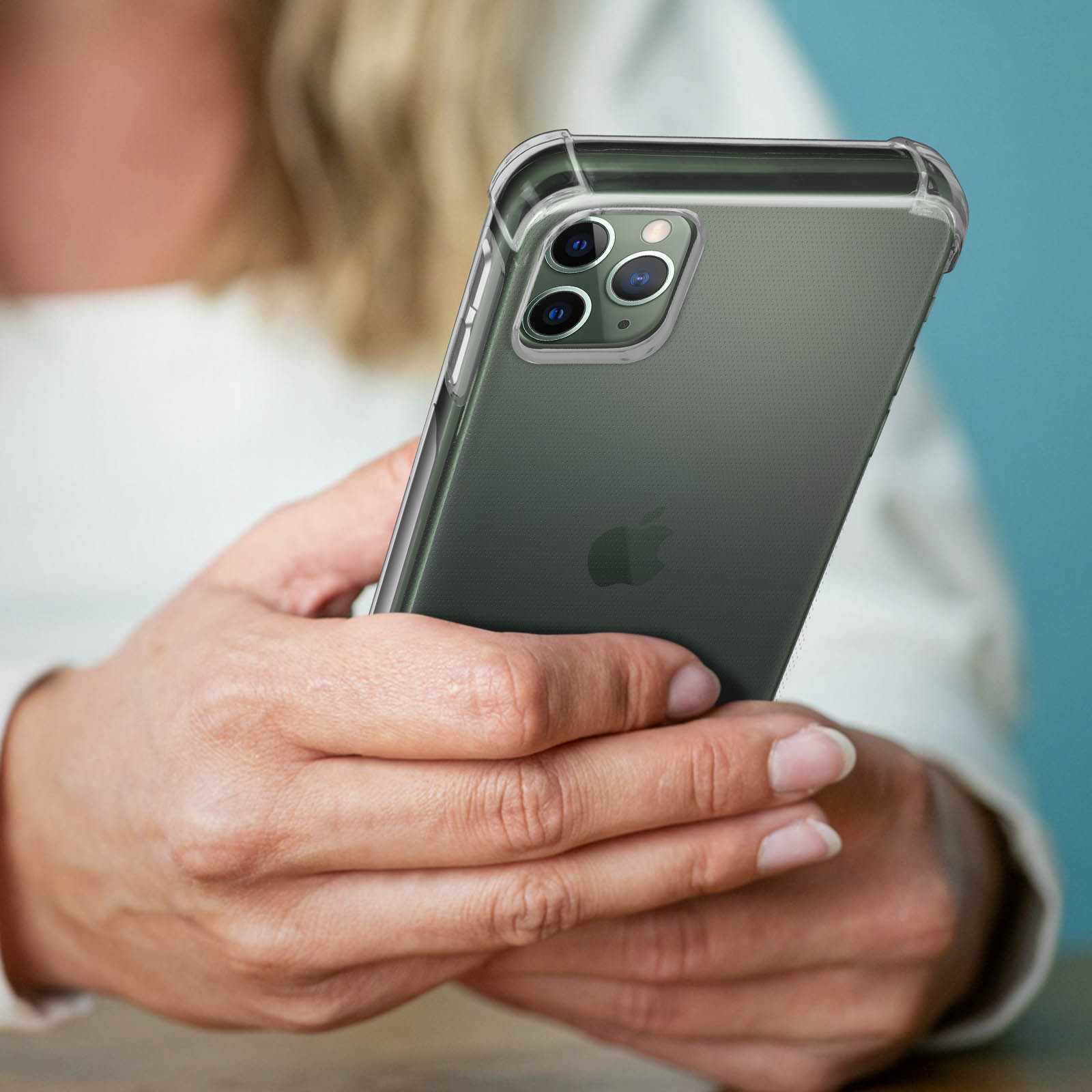 Persona che tiene in mano uno smartphone. Il telefono ha una custodia trasparente. Lo sfondo è un muro blu.