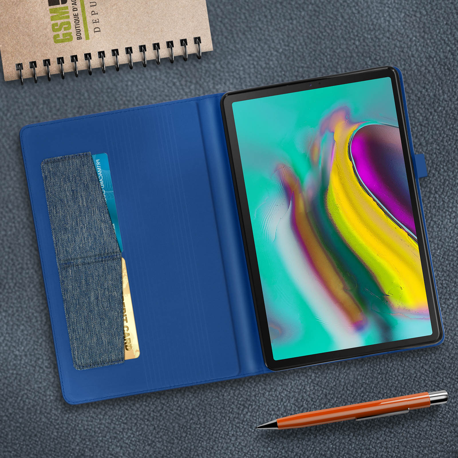 Un tablet in una custodia blu con una penna. Una carta di credito è nella custodia. Il tablet è su una superficie.