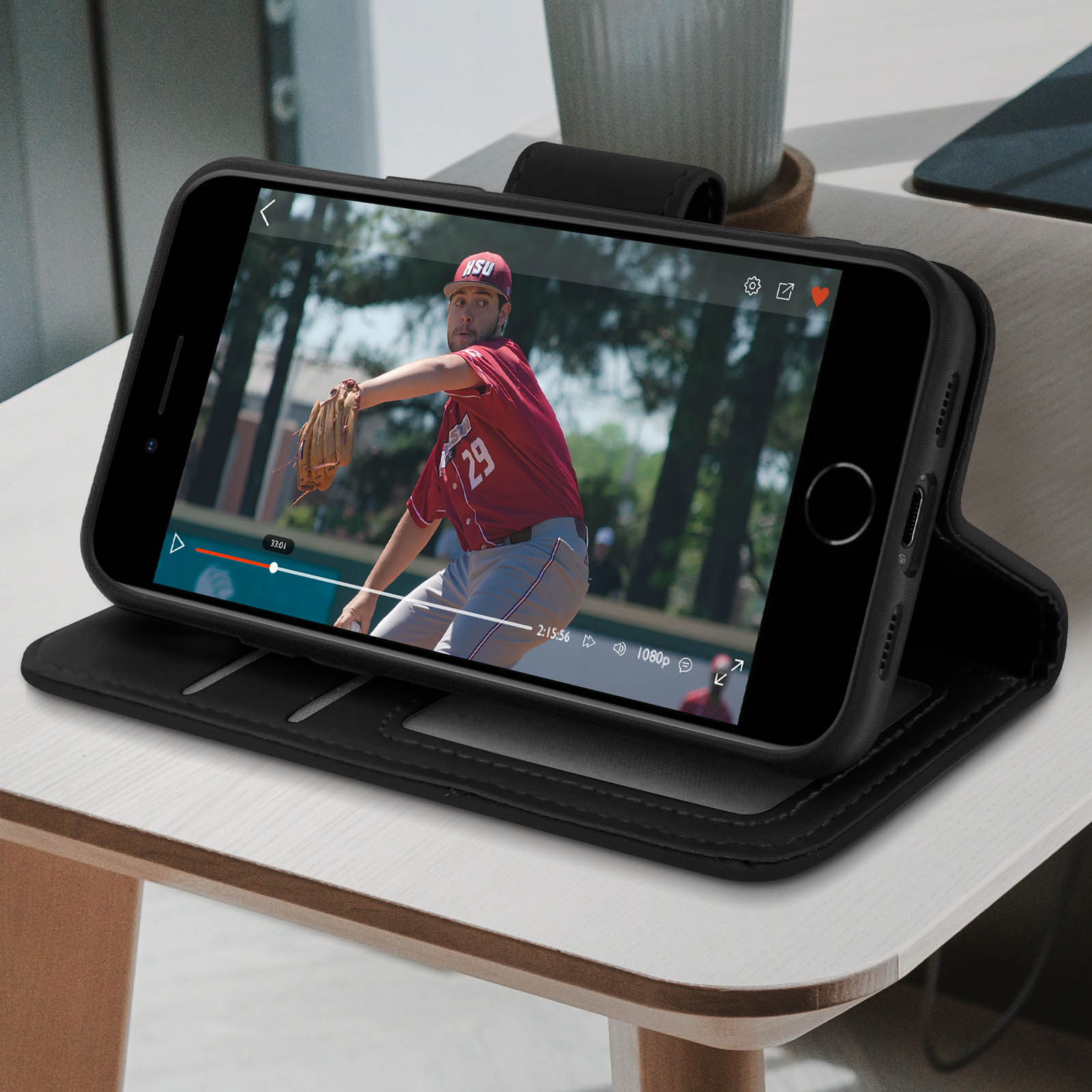 Téléphone dans un étui noir affichant une vidéo de match de baseball, reposant sur une surface en bois.