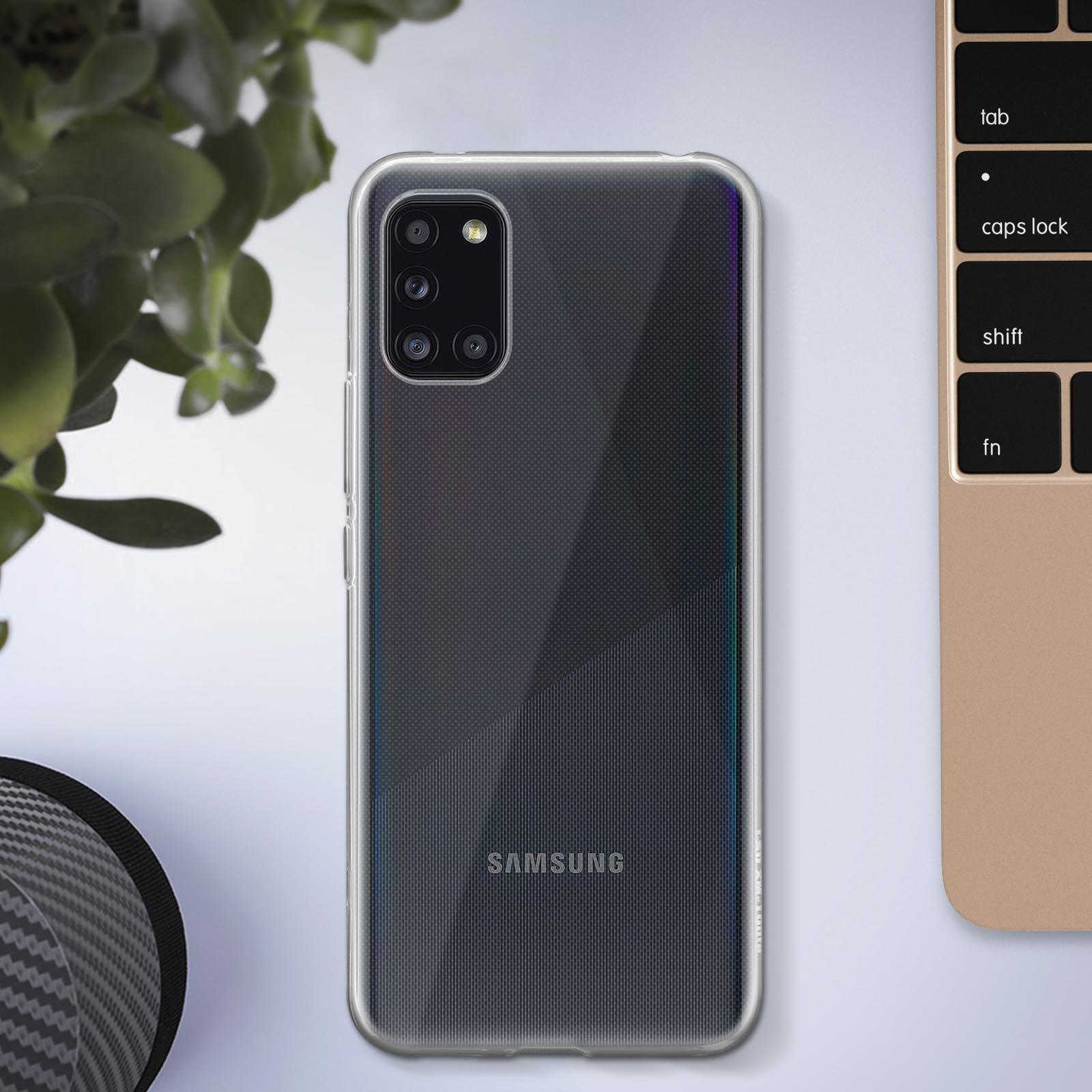 Un téléphone Samsung noir dans un étui transparent. Plante et clavier en arrière-plan.