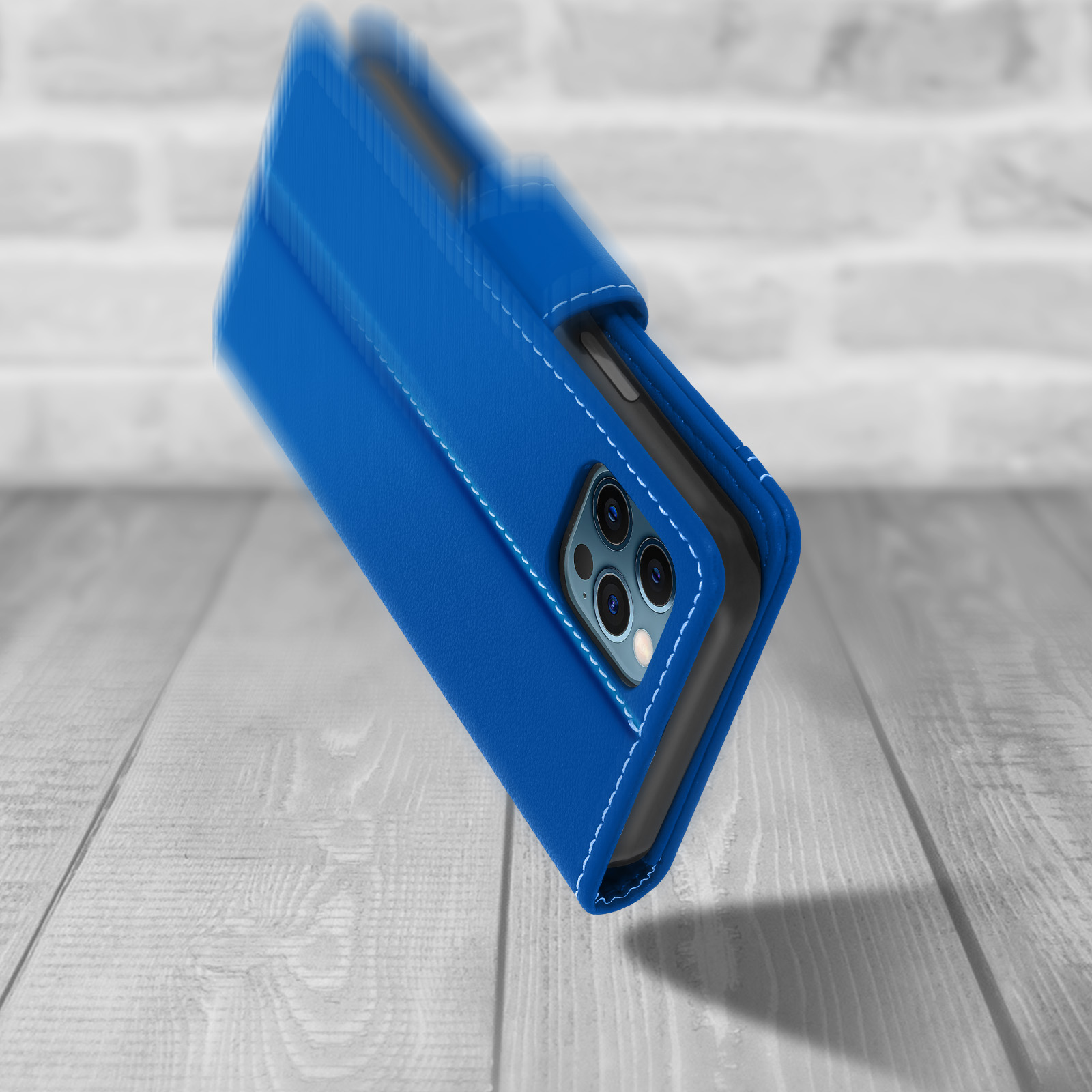 Blauwe telefoonhoes met witte stiksels. De telefoon is gekanteld en in beweging op een houten oppervlak.