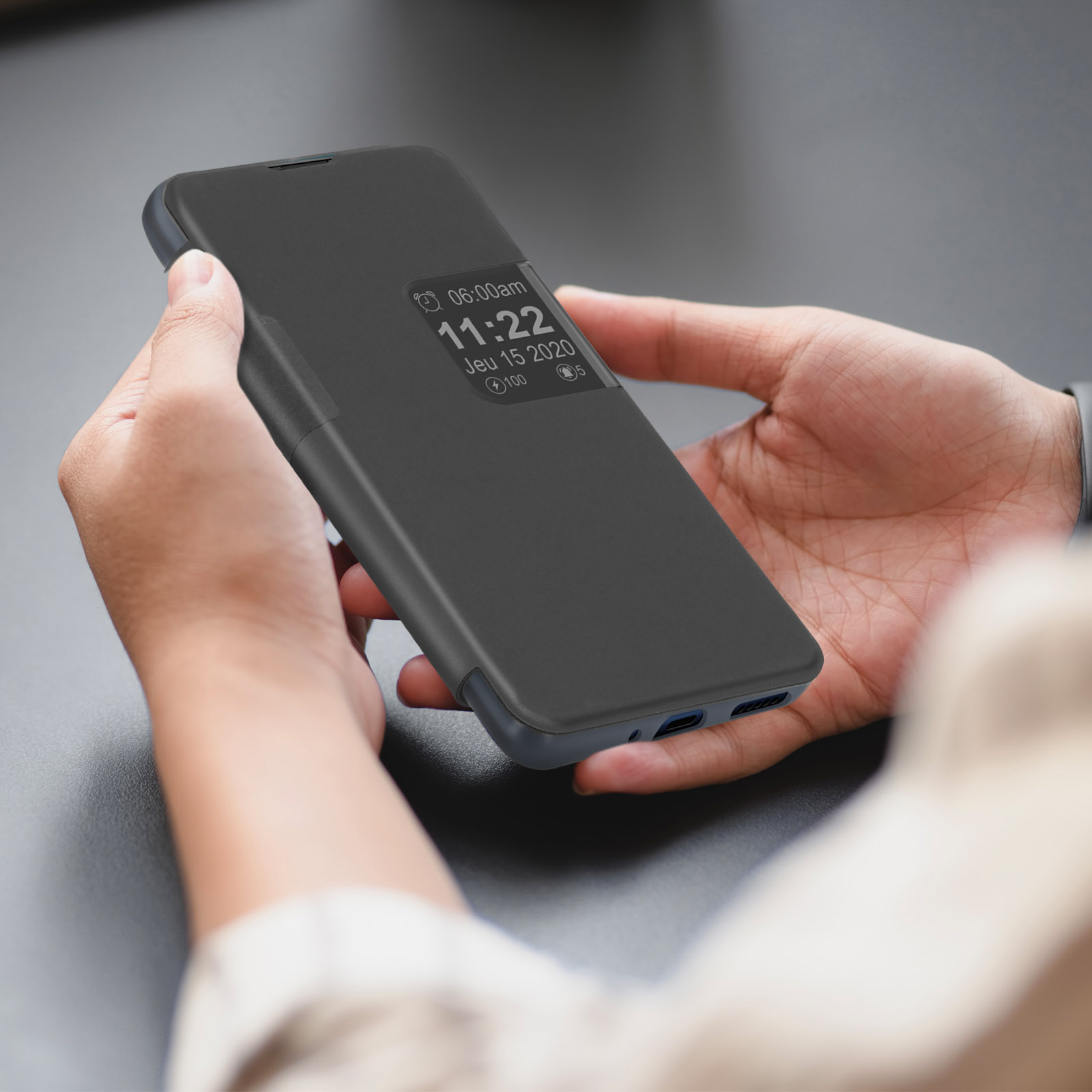 Una persona tiene in mano una custodia nera per telefono. Lo schermo mostra l'ora e la data.