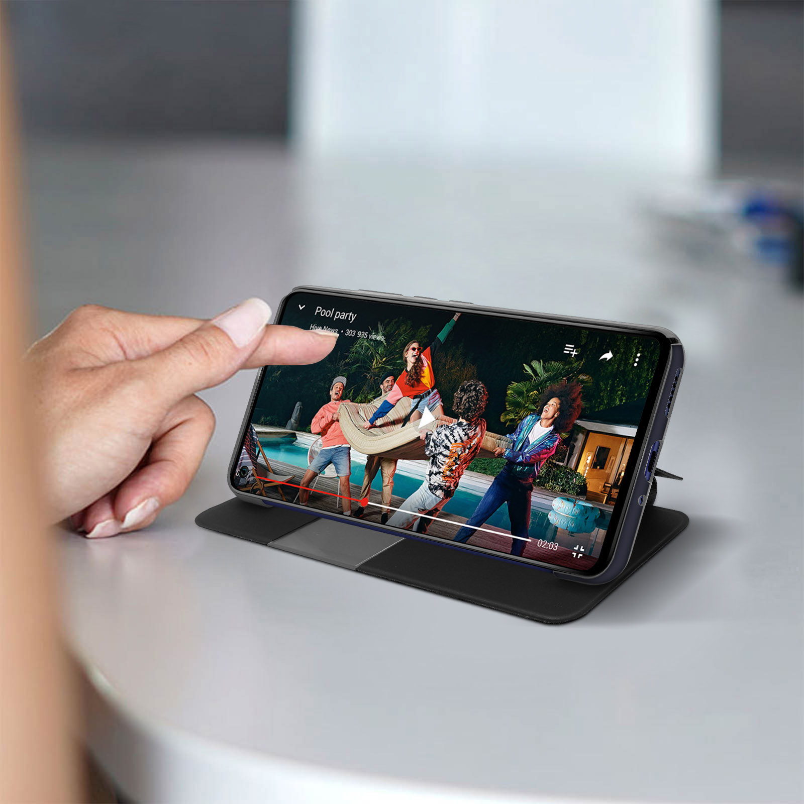 Persona che tocca un telefono con un video in riproduzione. Il telefono poggia su una custodia.