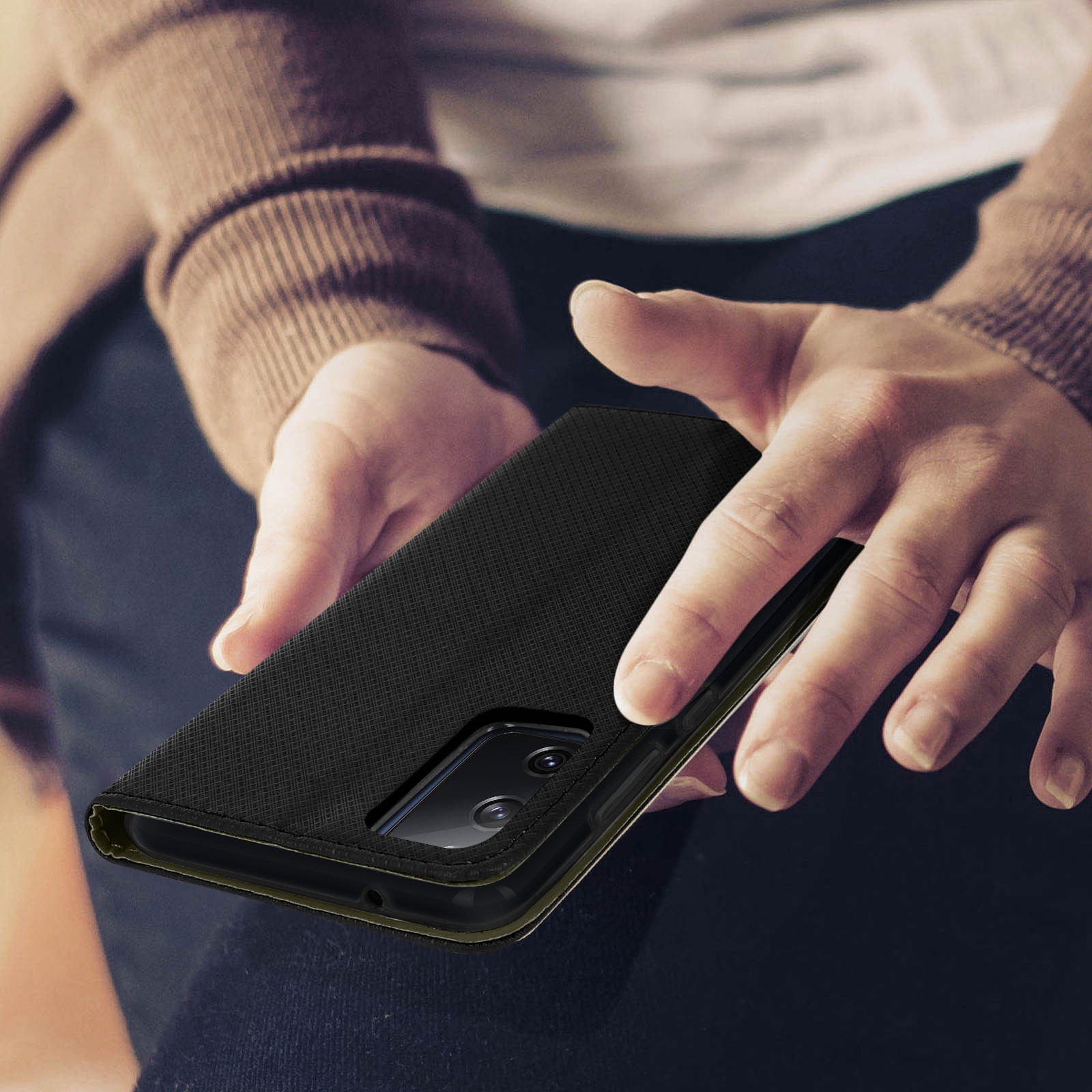 Handen van een persoon die een gesloten zwarte telefoonhoes vasthoudt. Donkere achtergrond, lage hoek.